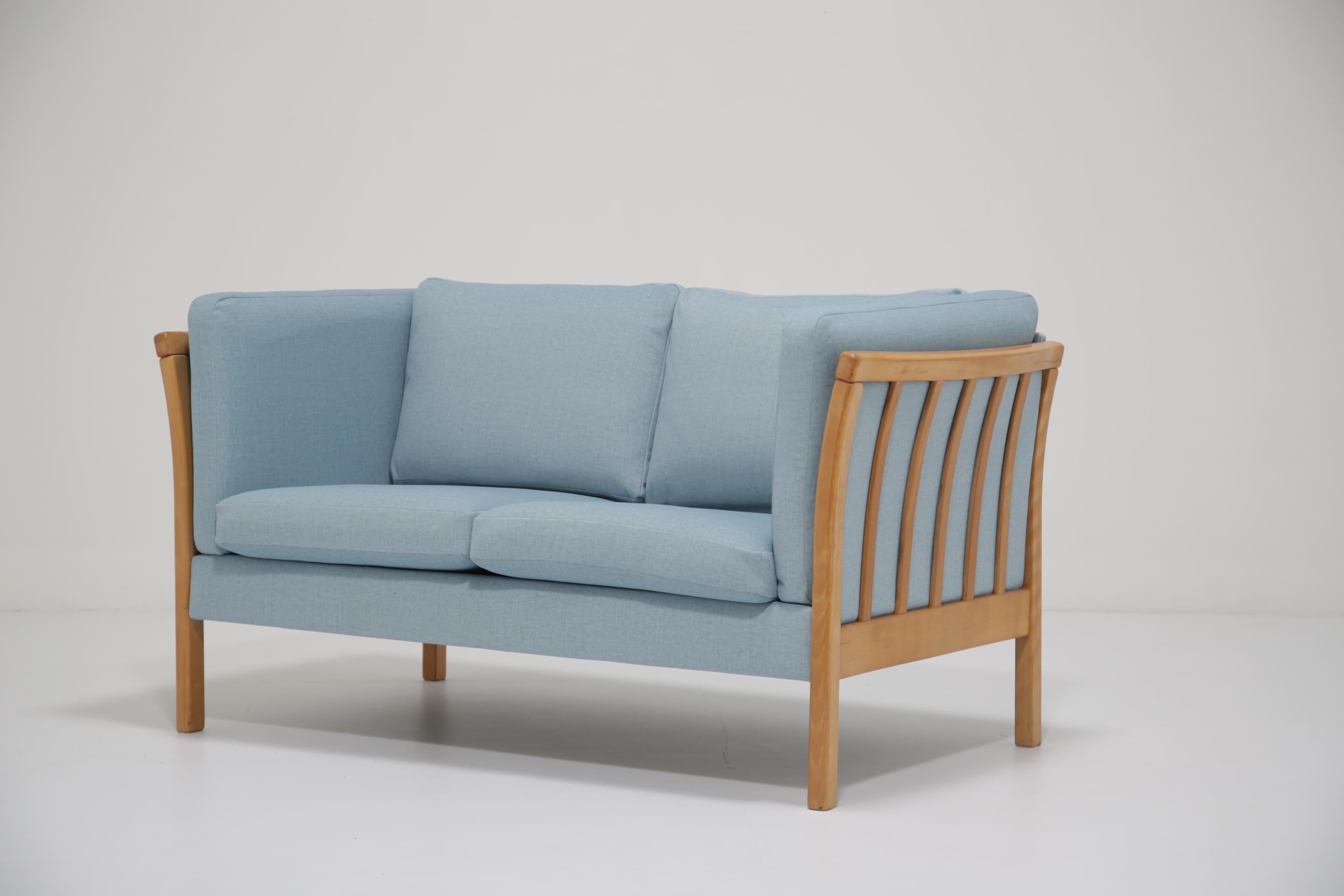 Questo bellissimo divano a due posti era originariamente in pelle nera, che purtroppo era ormai troppo vecchia per essere recuperata, quindi lo abbiamo rivestito con un delizioso tessuto blu morbido che si sposa perfettamente con il legno di questo