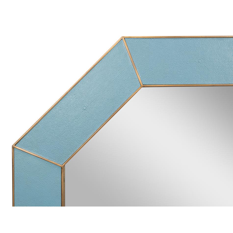 Enveloppé dans un cuir gaufré bleu chambray vibrant, le cadre est orné d'accents dorés fabriqués à la main, ajoutant une touche de sophistication intemporelle. En son centre, le miroir biseauté rehausse le design avec une profondeur accrue et une