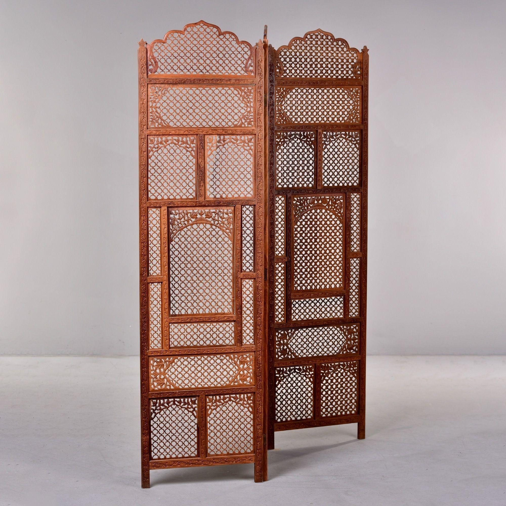 Circa 1970s folding three panel Indian carved wood floor screen or room divider. Loads of classic bohemian style with this intricately carved screen that features open work lattice patterns, floral vines, arched top and footed base. Very sturdy and