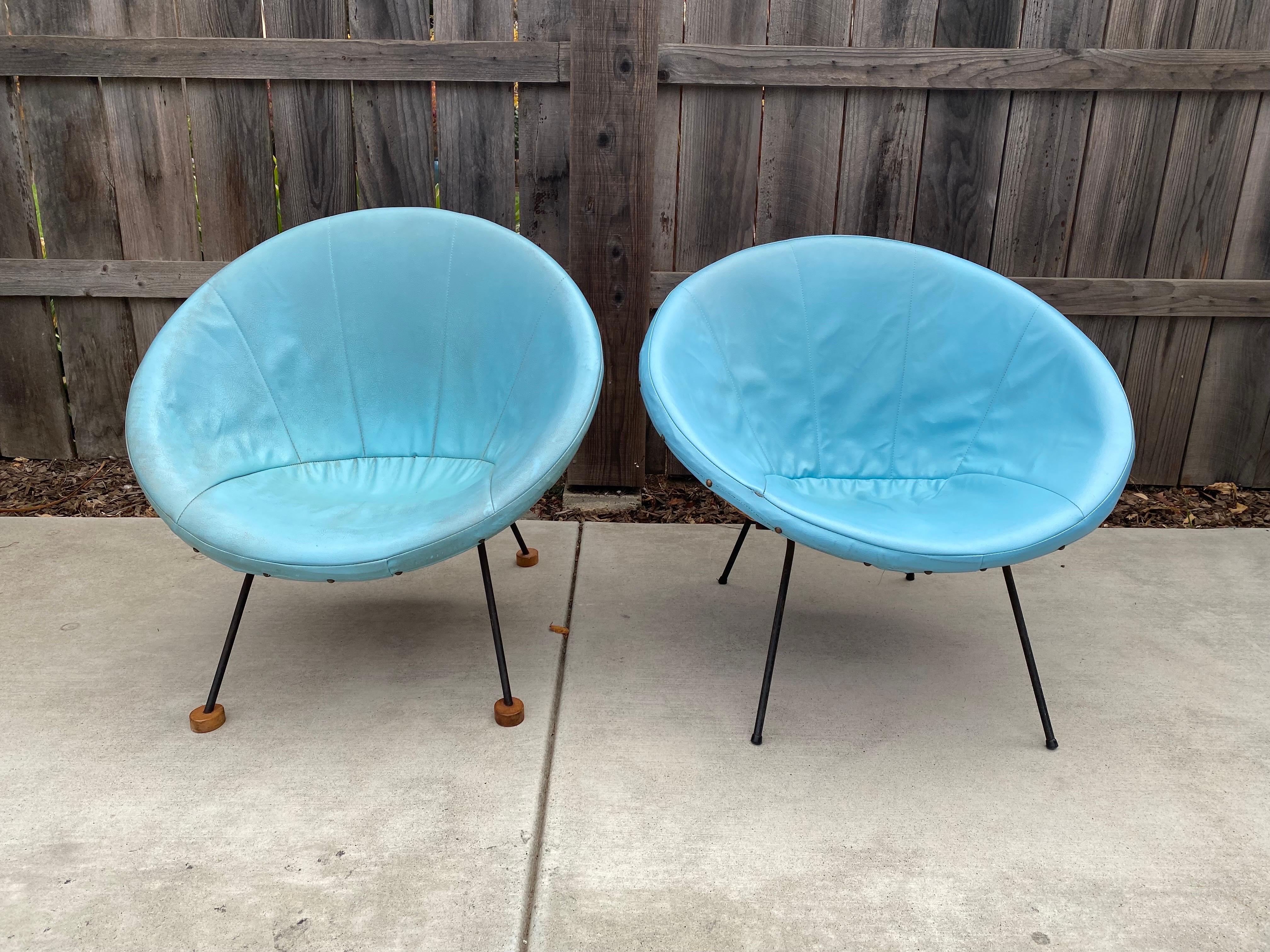 For sale we have a stunning pair of midcentury rattan club chairs, scoop chairs or side chairs, both with their original turquoise faux leather or vinyl seat covers. Both chairs sit on a cast iron frame with one chair having wooden feet. A stunning