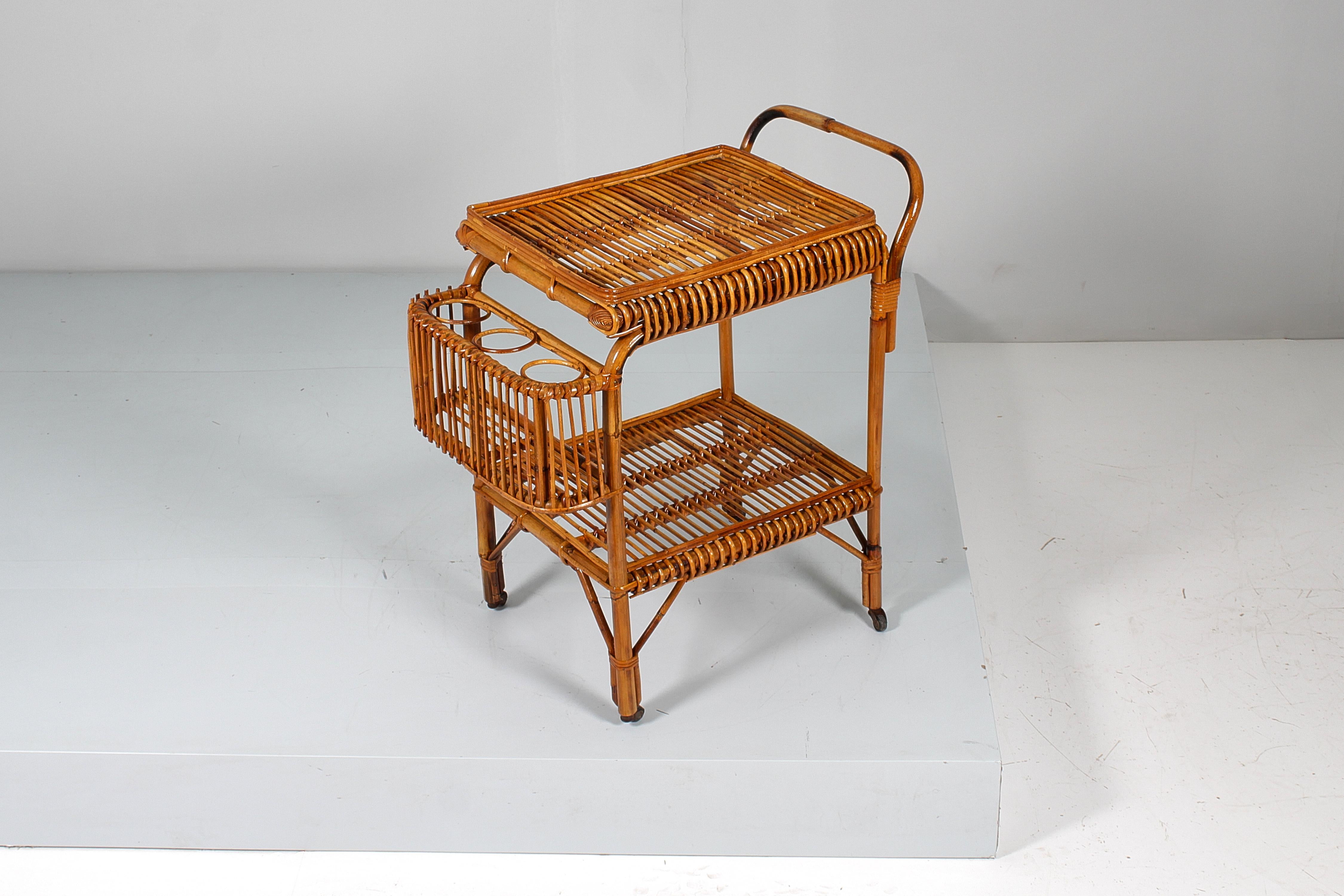 Elegant and rustic bar trolley in bamboo cane and rattan, with two large tops, handle, protruding bottle holder, resting on four wheels. Attributable to Bonacina, Italian manufacture from the 1950s
Wear consistent with age and use.