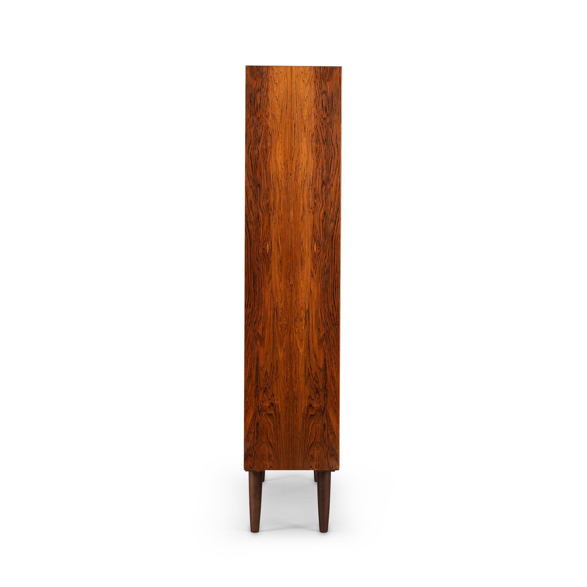 Danish tall bookcase in beautiful hardwood veneer. Designed by Carlo Jensen and made by Hundevad & Co. This bookcase is in very good vintage condition and has a total of 7 height-adjustable shelves.
  