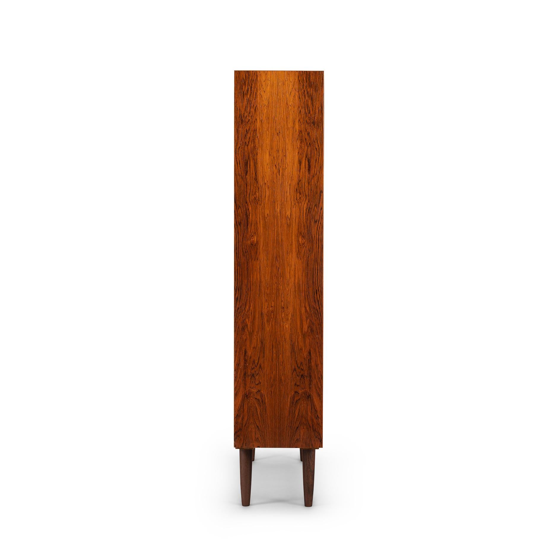 Danish tall bookcase in beautiful hardwood veneer. Designed by Carlo Jensen and made by Hundevad & Co. This bookcase is in very good vintage condition and has a total of 8 height-adjustable shelves.
  