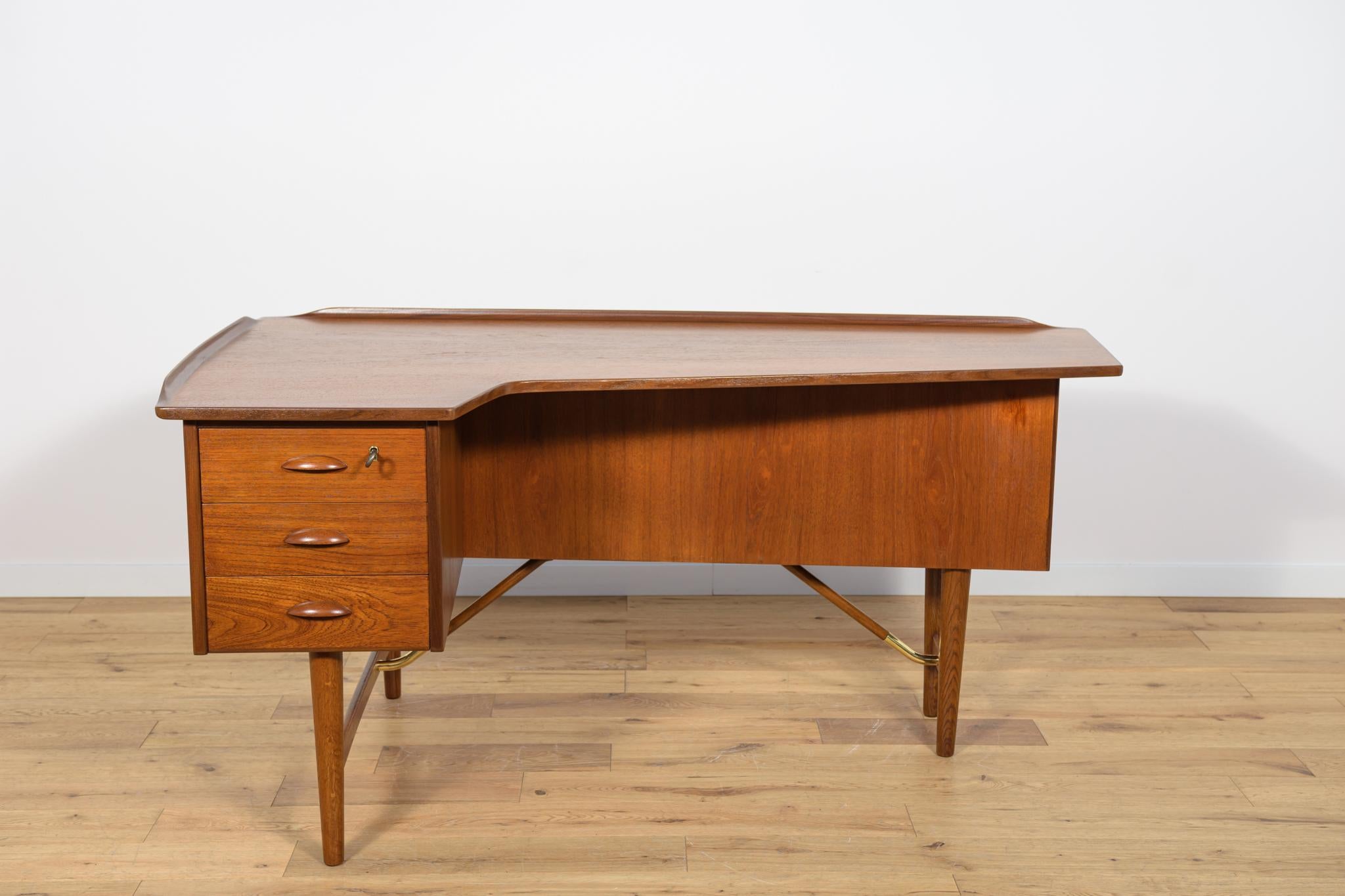 Precioso escritorio esquinero de teca, obra de Peter Lovig Nielsen y fabricado en la década de 1970. Es de teca con detalles de latón. Consta de tres cajones en la parte delantera, un espacio abierto para libros y una barra con cerradura en la parte
