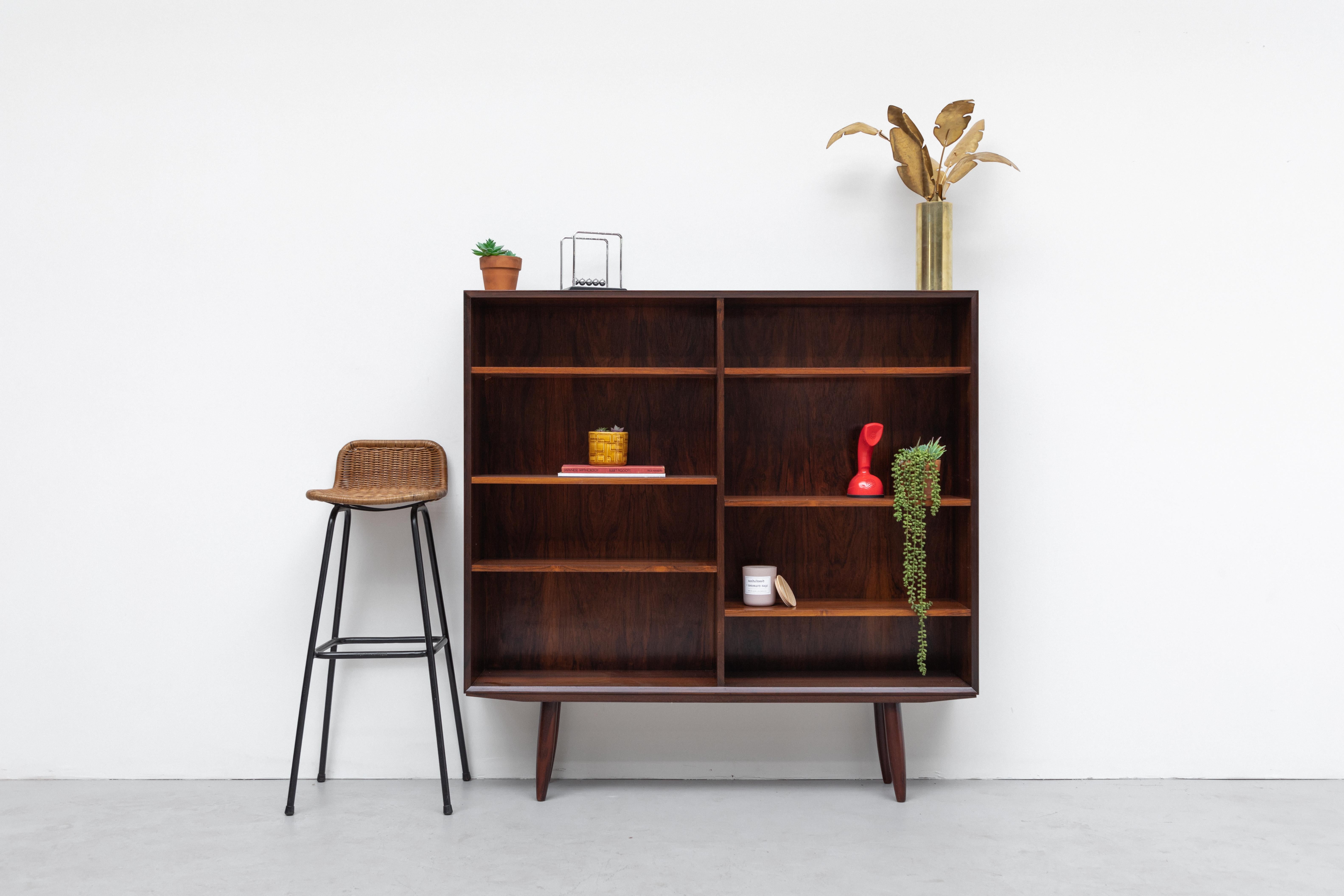 Mid-century rosewood bookcase with angled tapered legs. Lightly refinished with six adjustable shelves. In overall impressive condition with some wear consistent with age and use. Visible shadows where original shelves were place, dark lines are