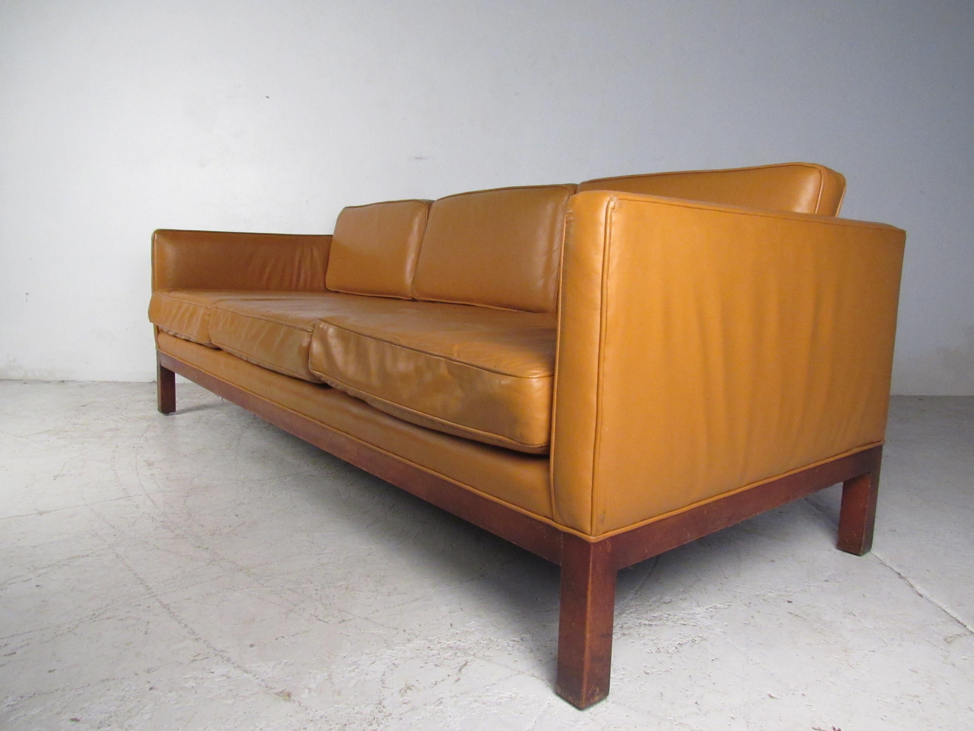 This impressive vintage modern sofa boasts six overstuffed removable cushions ensuring maximum comfort in any seating arrangement. A sleek design covered in tan leather that sits on a sturdy walnut base. This stunning midcentury sofa adds style and