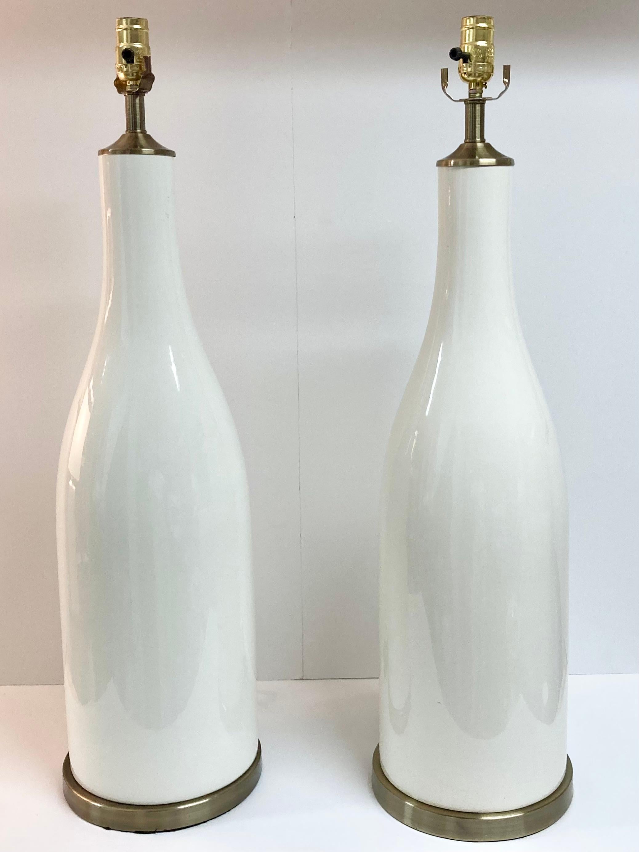 Paire de lampes de table du milieu du siècle en céramique émaillée blanche en forme de bouteille. De jolies bases en bronze mettent en valeur la paire de formes en céramique de grande taille. Il suffit d'ajouter des harpes et votre style d'ombrage