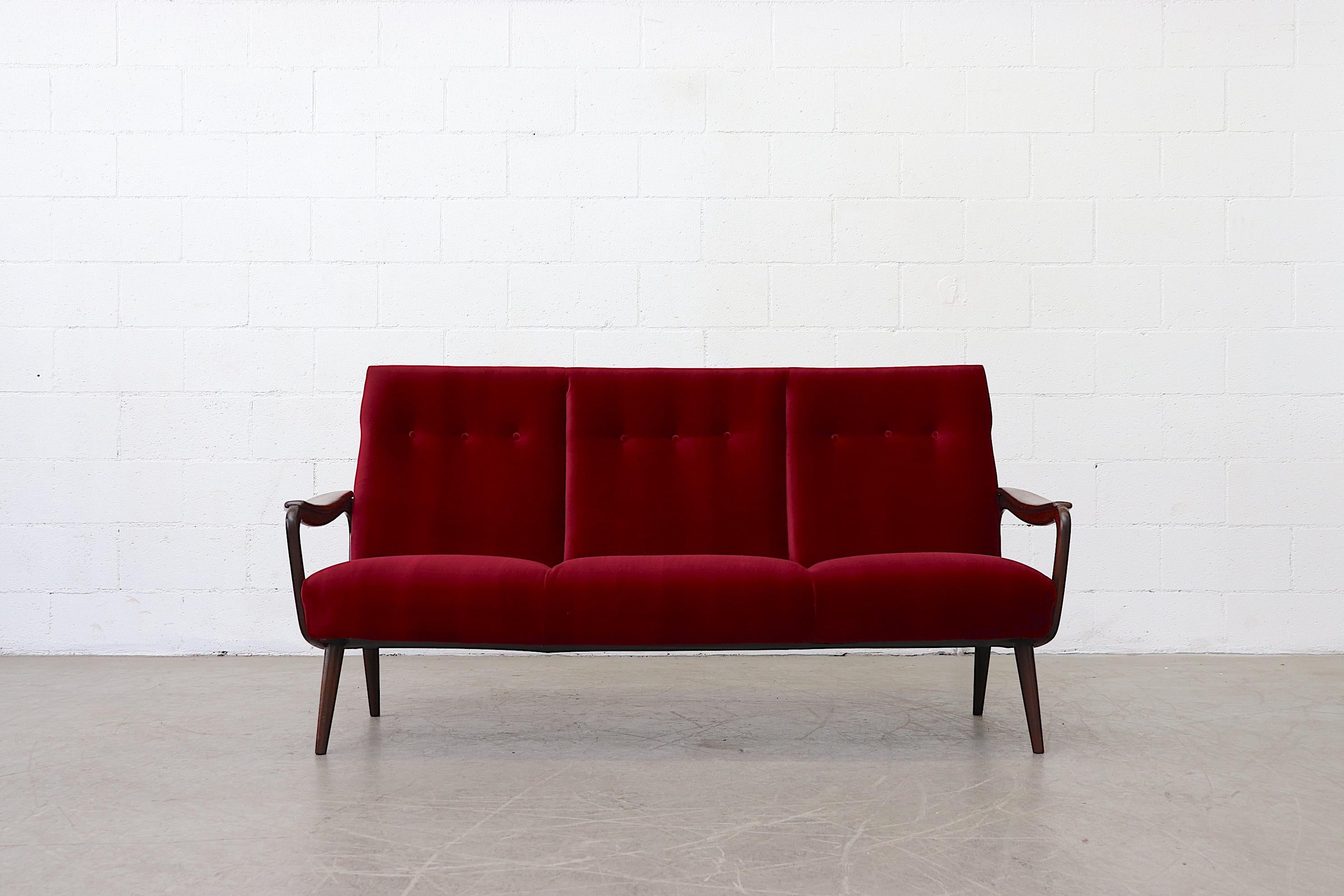 Dutch mid-century, three-seater sofa with organic carved arm rests and legs in a characteristic of the post-war style esthetic, reminiscent of the output of Dutch furniture maker Bovenkamp . Fresh garnet colored upholstery with refinished frame.