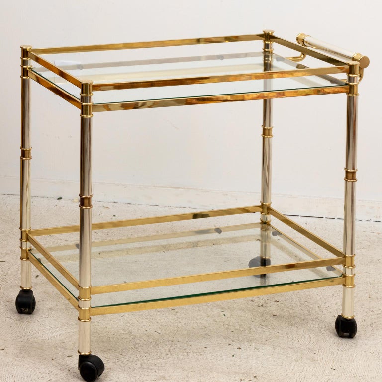 Circa 1970s Mid-Century Modern style brass and chrome two tiered glass bar cart on casters. Made in the United States. Please note of wear consistent with age. The piece has been recently shined and lacquered.