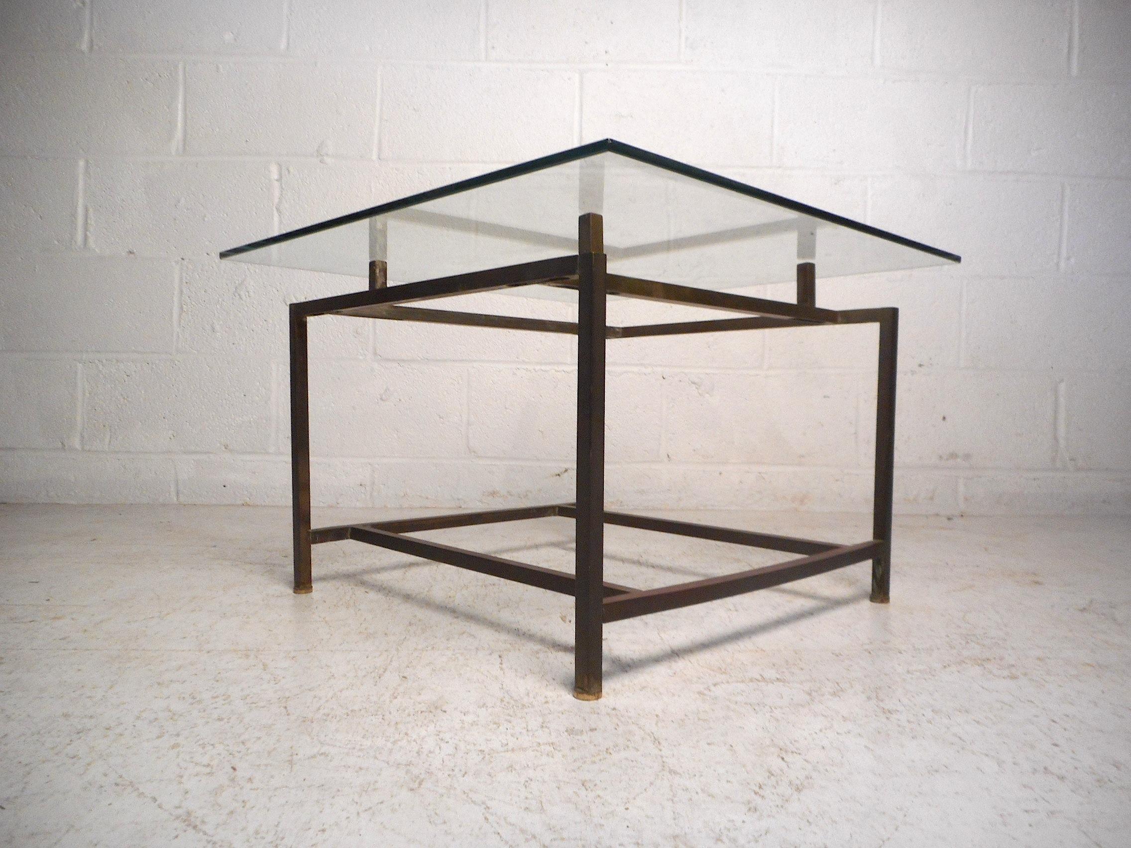 This unusual midcentury end table features a minimalist brass frame which supports a square piece of beveled glass which serves as the tabletop. An interesting and eye-catching addition to any modern interior. Please confirm item location with