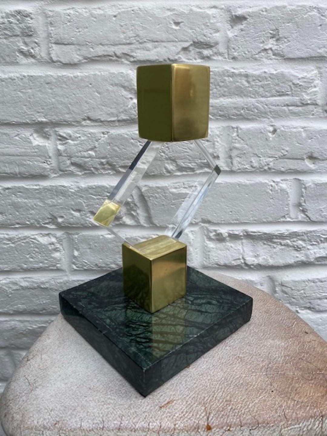 Mid-century brass and lucite sculpture on green marble base, French 1970s

Beautiful Mid-Century Modern brass and lucite sculpture. Rectangular lucite block, appears to be pivotting on its corners between two brass cubes. On a green marble base.