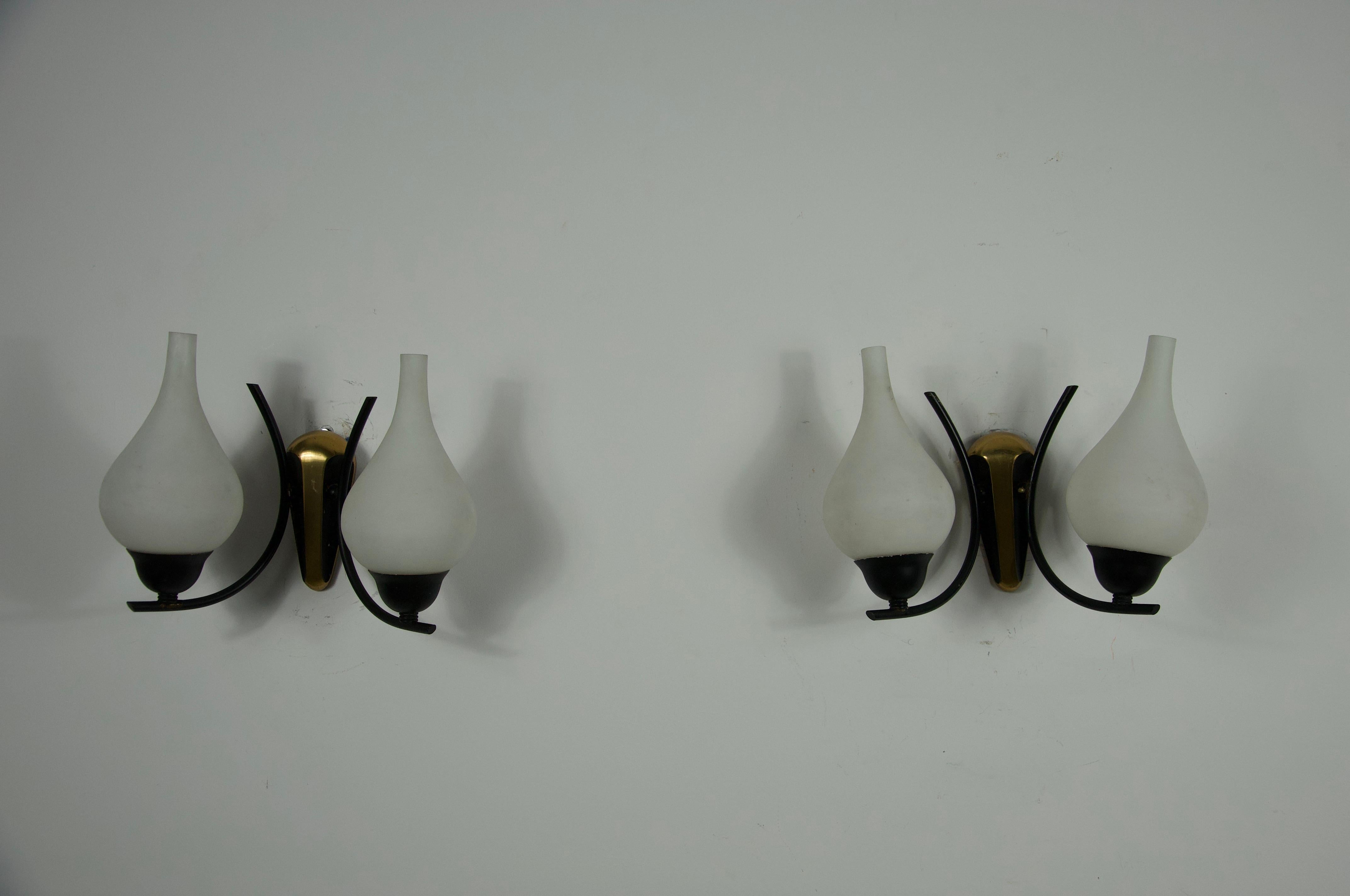 Este elegante par de apliques de mediados de siglo fue diseñado y fabricado por Stilnovo en Italia durante la década de 1960. Cada lámpara presenta un escultural brazo de latón y una pantalla de cristal opalino suavemente curvada, que ofrece una luz