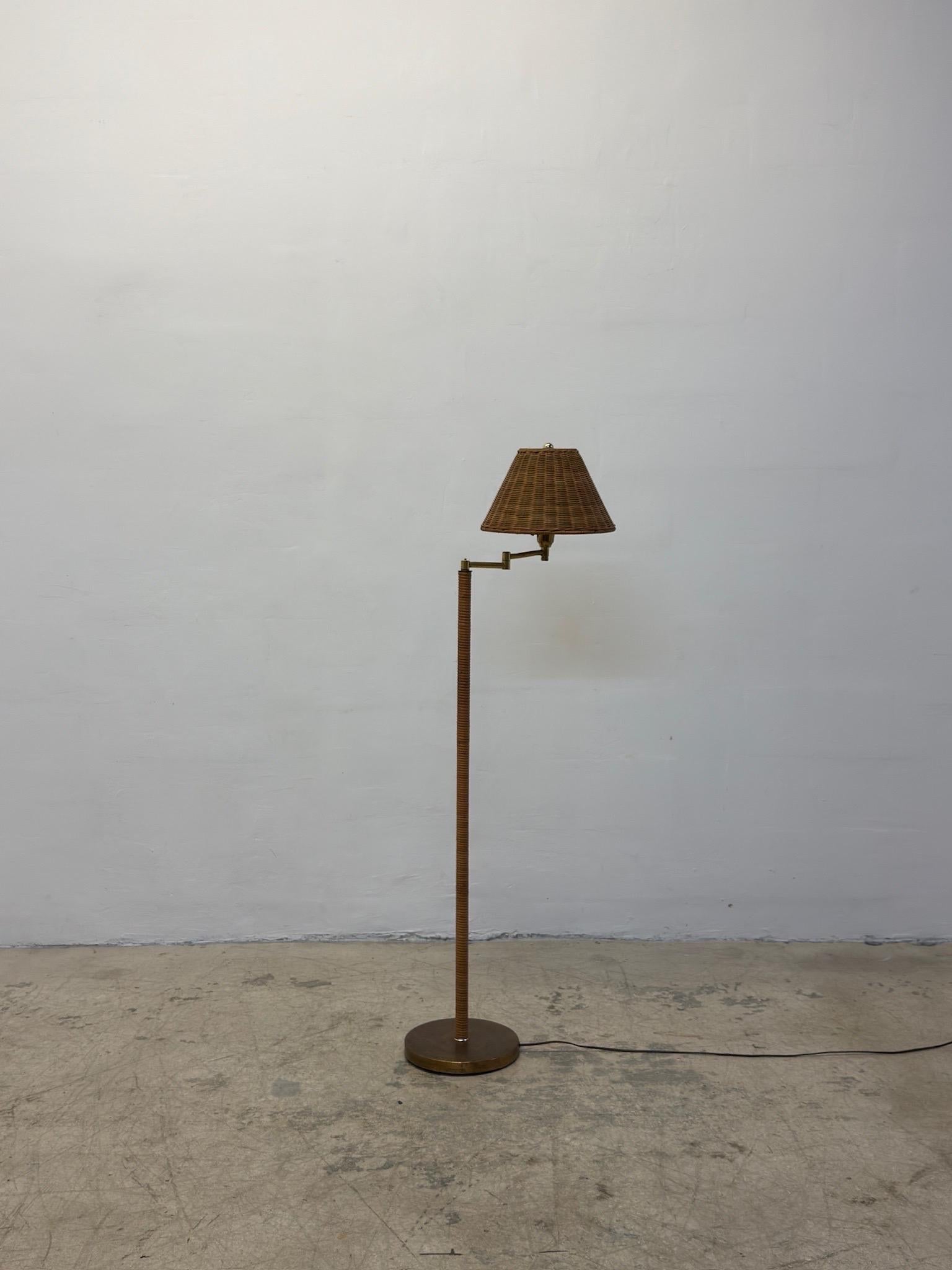 Rattan wrapped mid-century floor lamp with a brass base, adjustable arm and a wicker shade circa 1960s.