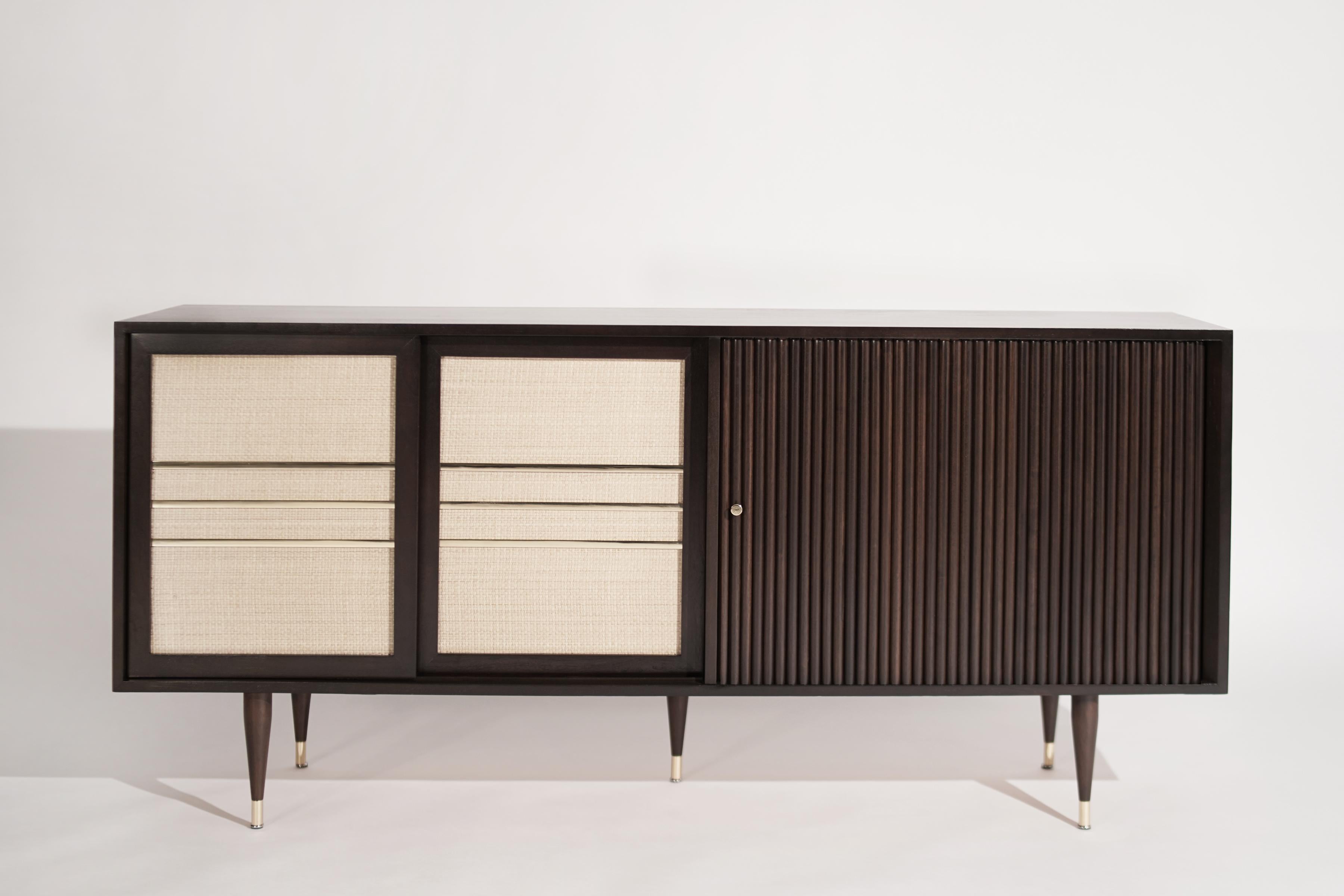 A super unique Mid-Century Modern credenza, circa 1950-1959. Executed in walnut, it features newly basket-weaved sliding doors with brass details and sabots. The left door opens up to reveal shelving, meanwhile, the right tambour door provides large