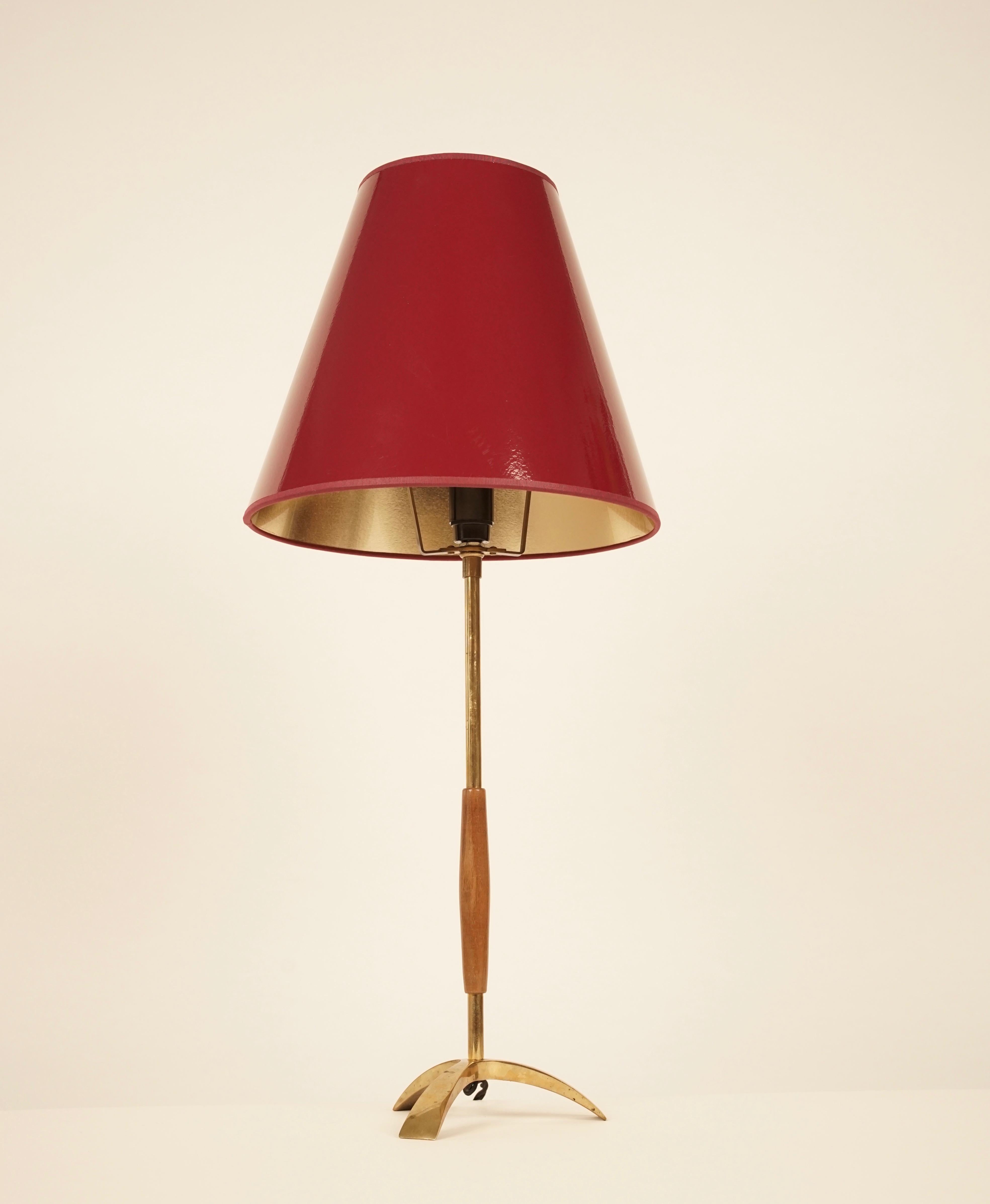 Eine hohe, einfache und elegante Tischleuchte von Kalmar. Hergestellt aus Messing und Holz. Die Lampe hat jetzt einen neuen weinroten Schirm mit reflektierendem Goldfutter. 
Das goldene Futter setzt schöne Akzente im Licht.
