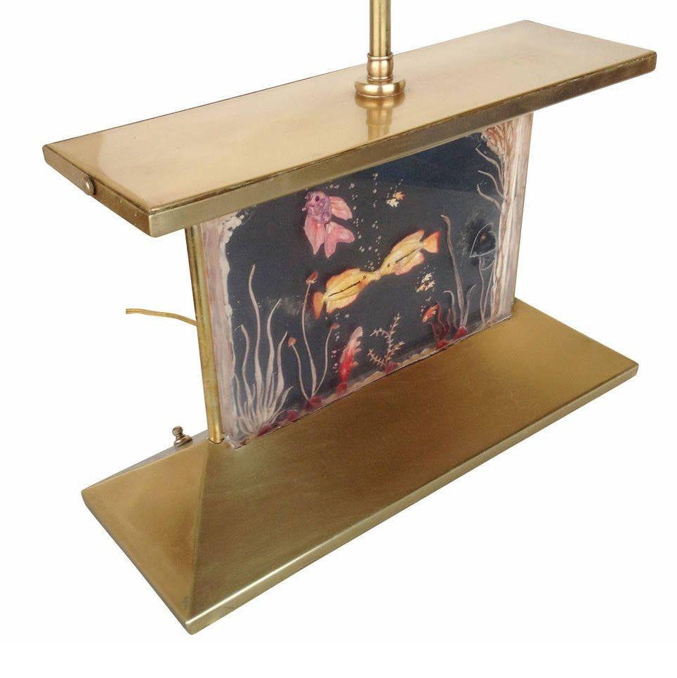 Mid-century brass aquarium lamp with original shade. This piece features an East Asian-inspired brass form constructed of brass with a hand-formed light-up acrylic aquarium window. The window shows a school of fish swimming around with a pair of