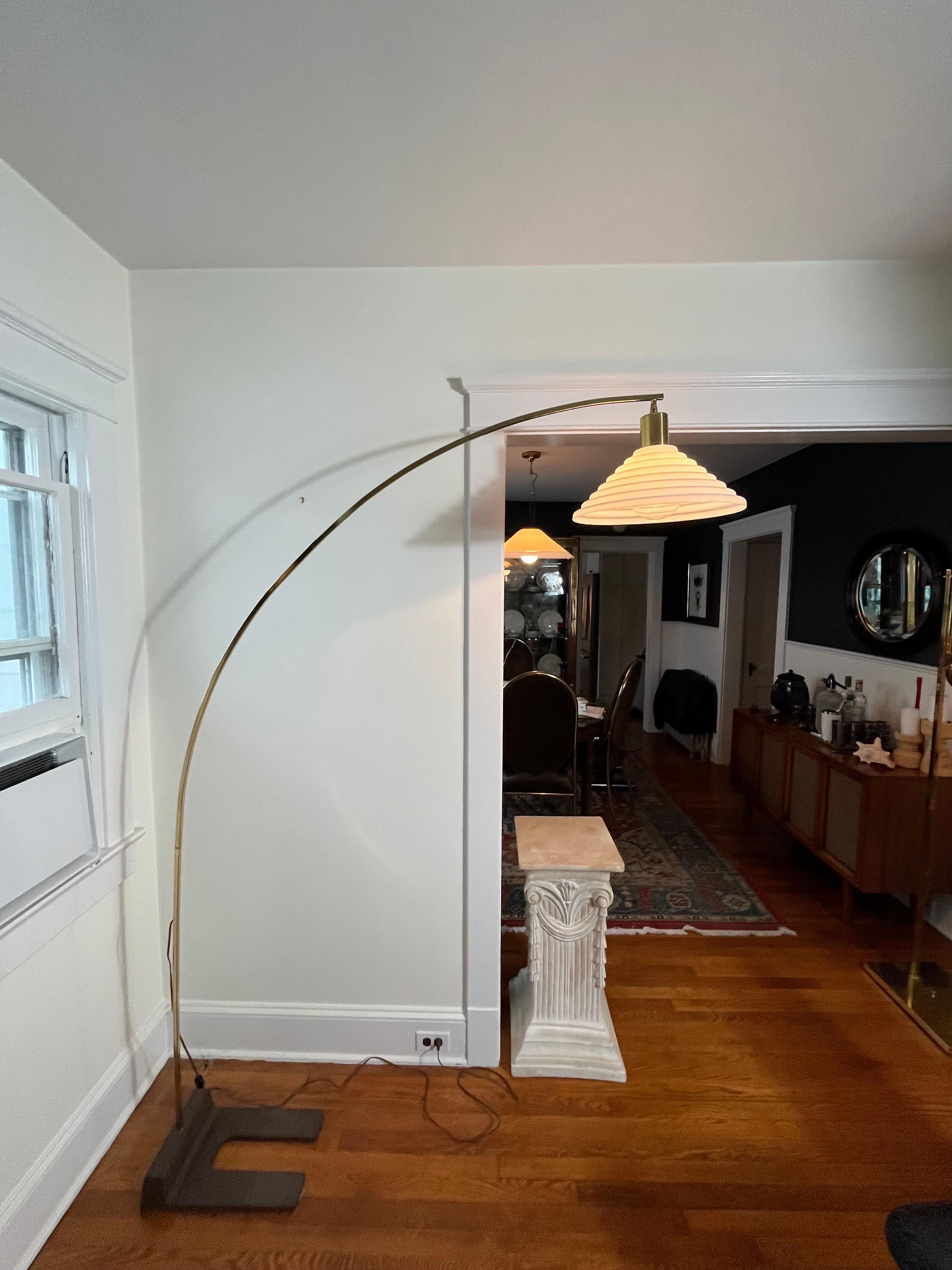 Classic simplicity in this brass arc floor lamp. Stepped pagoda style glass shade in the style of Guzzini. Square tubular frame disassembles into 3 pieces for ease in movement. Heavy iron horseshoe base.