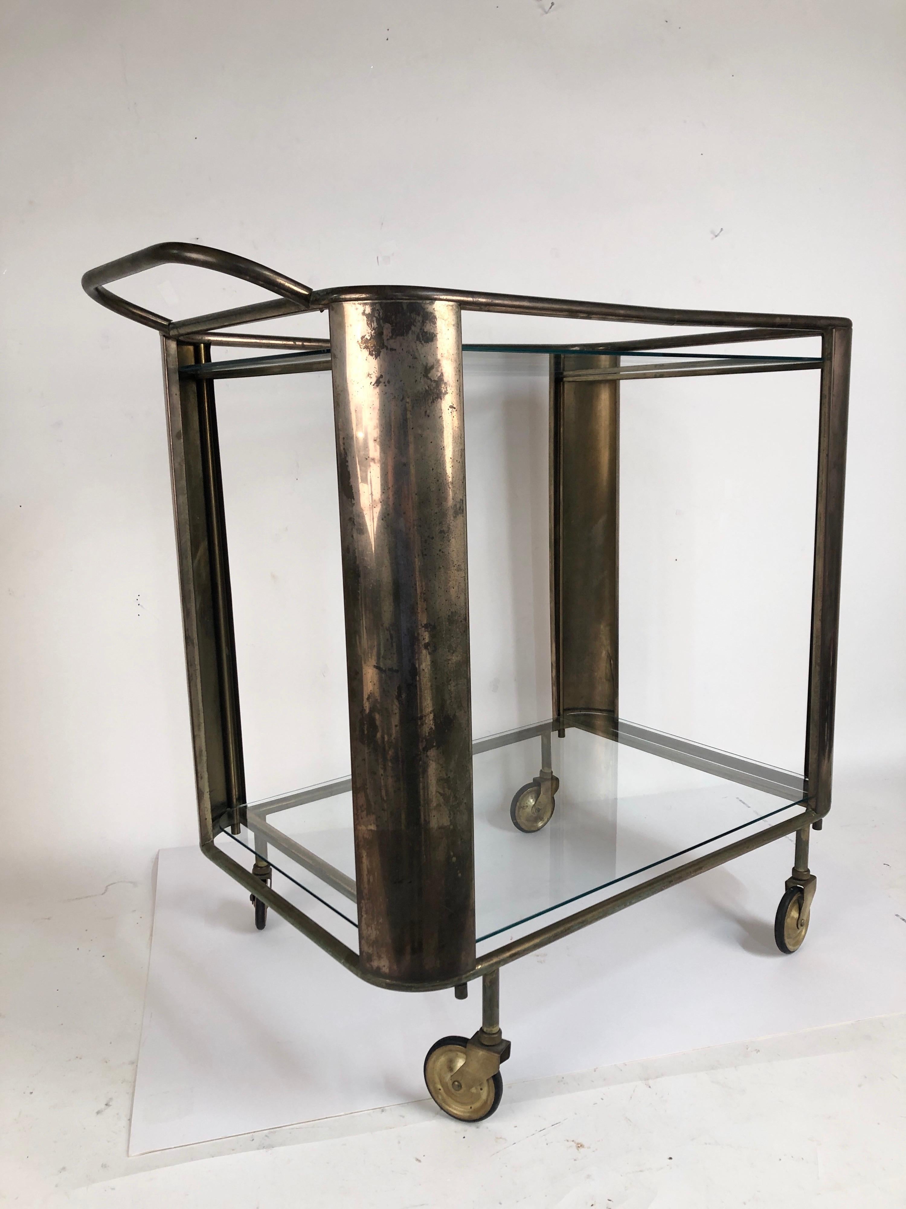 A nice Mid-Century Modern brass bar cart with two glass shelves and nice decorative wheels. Untouched patina surface.