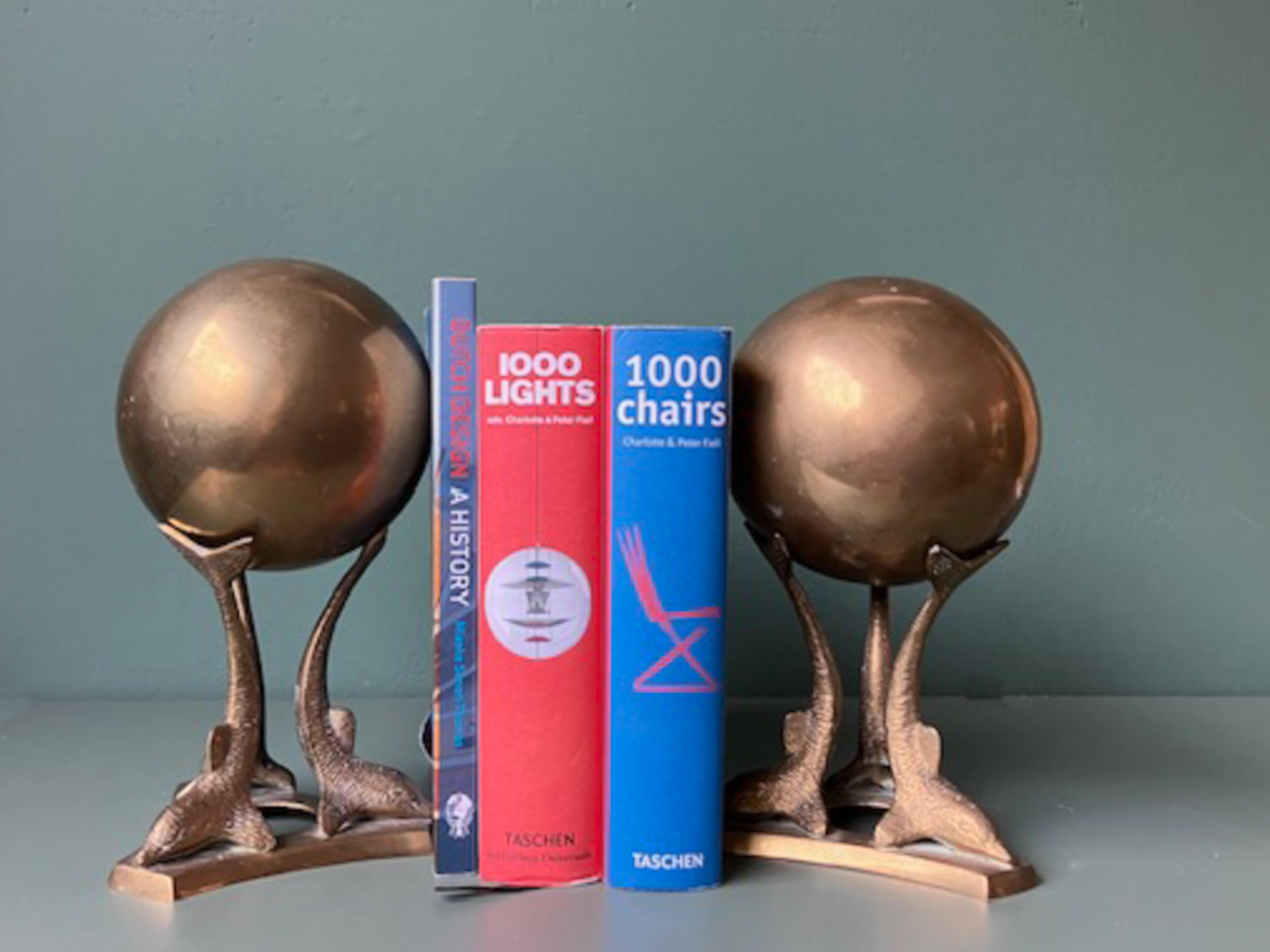 Unique pair of bookends, each of three dolphins holding a big globe They are made of brass. It is a beautiful set for any home or office decor and would look great on table top or bookshelf. They are in vintage condition (they havemarks and wear