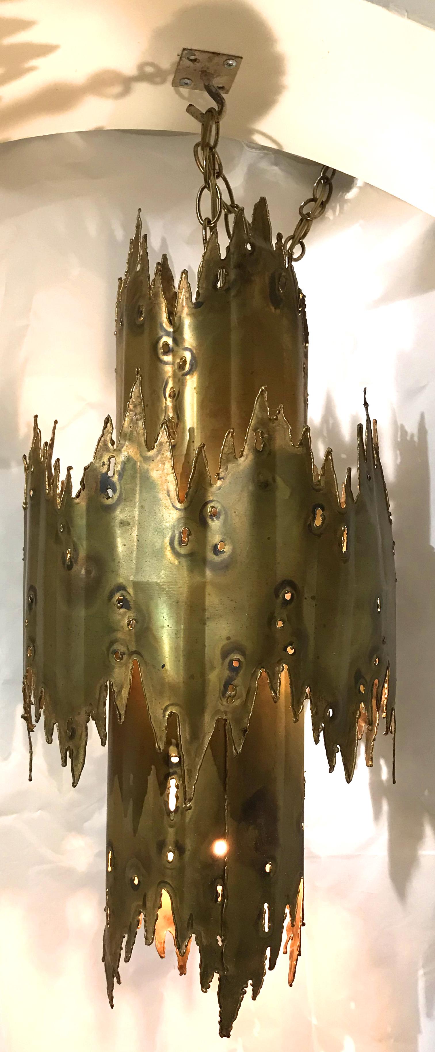 A fine example of a torch cut brass chandelier in the form of two tiered concentric circles by metal sculptor Tom Greene, creating a beautiful patina with an oxyacetylene torch. 

Each piece that Tom Greene made was unique, no pieces are exactly