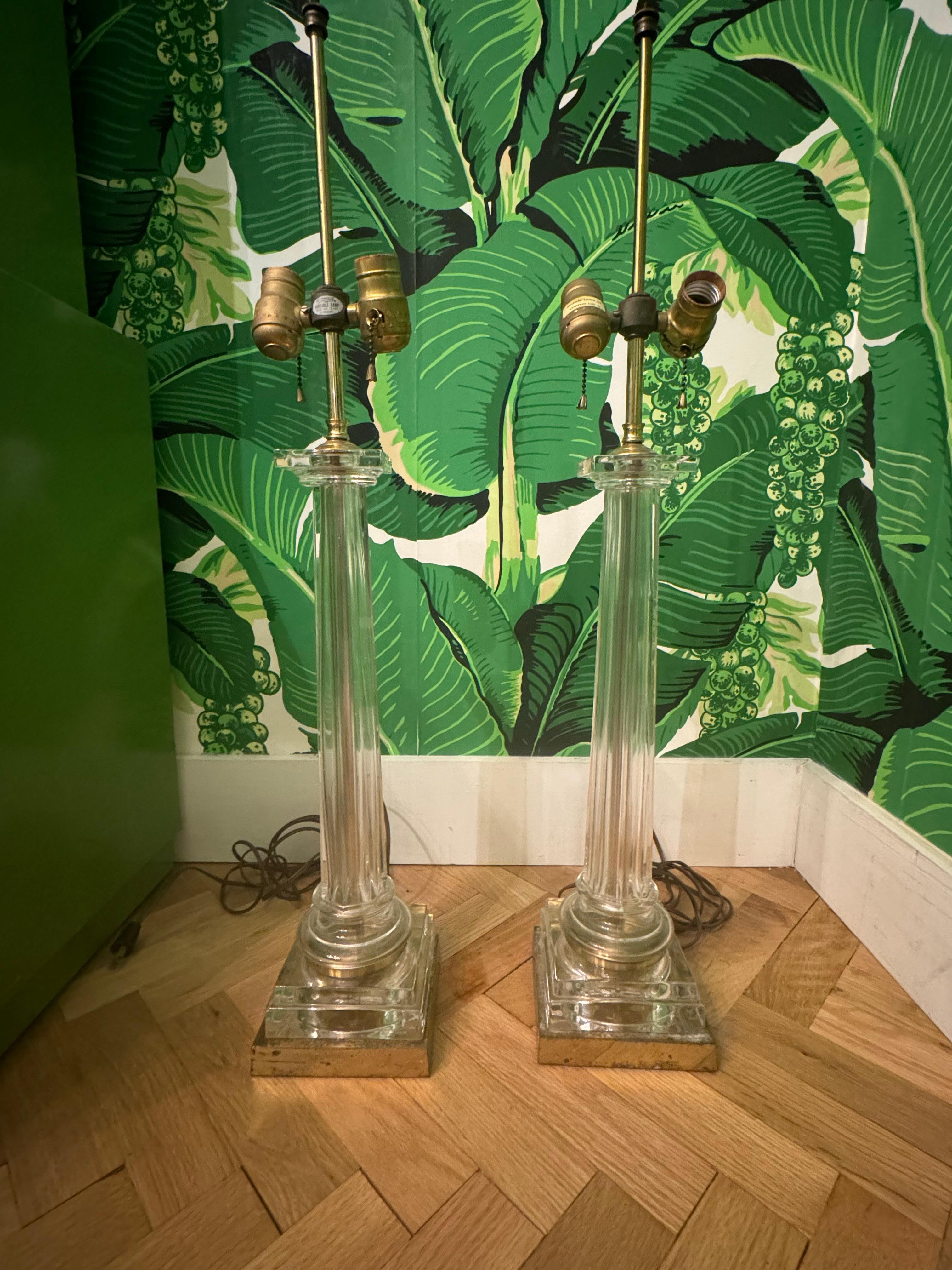 Pair of brass and crystal Roman column table lamps feature Corinthian capitals and fluted crystal shafts. Good condition with minor imperfections consistent with age, see photos for condition details. 
For a shipping quote to your exact zip code,
