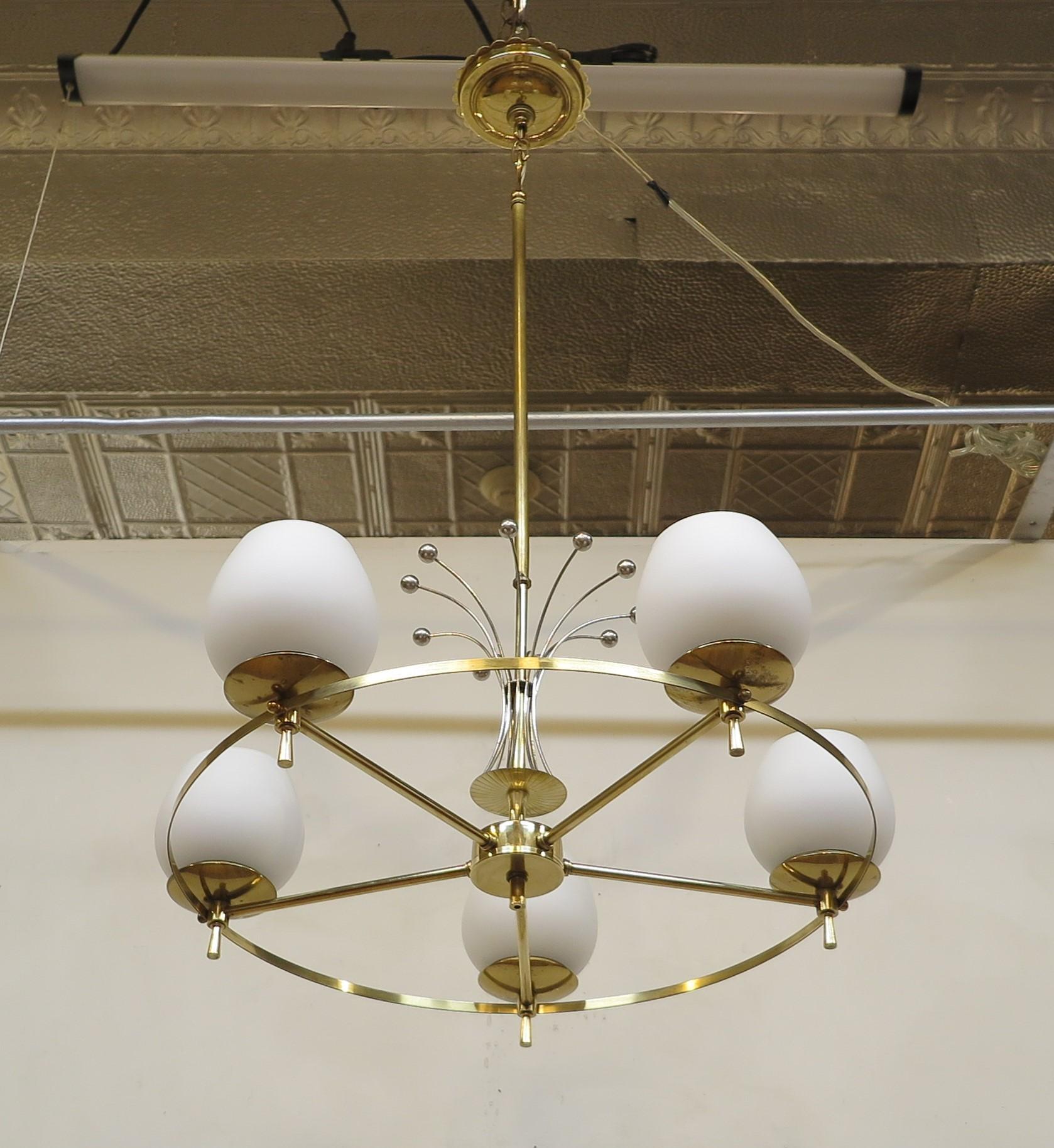 Midcentury brass and glass chandelier attributed to Gerald Thurston Lightolier. 
Brass ring holding five goblet frosted white shades set in brass cups with finial end caps to the bottom of each cup. Chrome wire burst toped with spheres set on brass