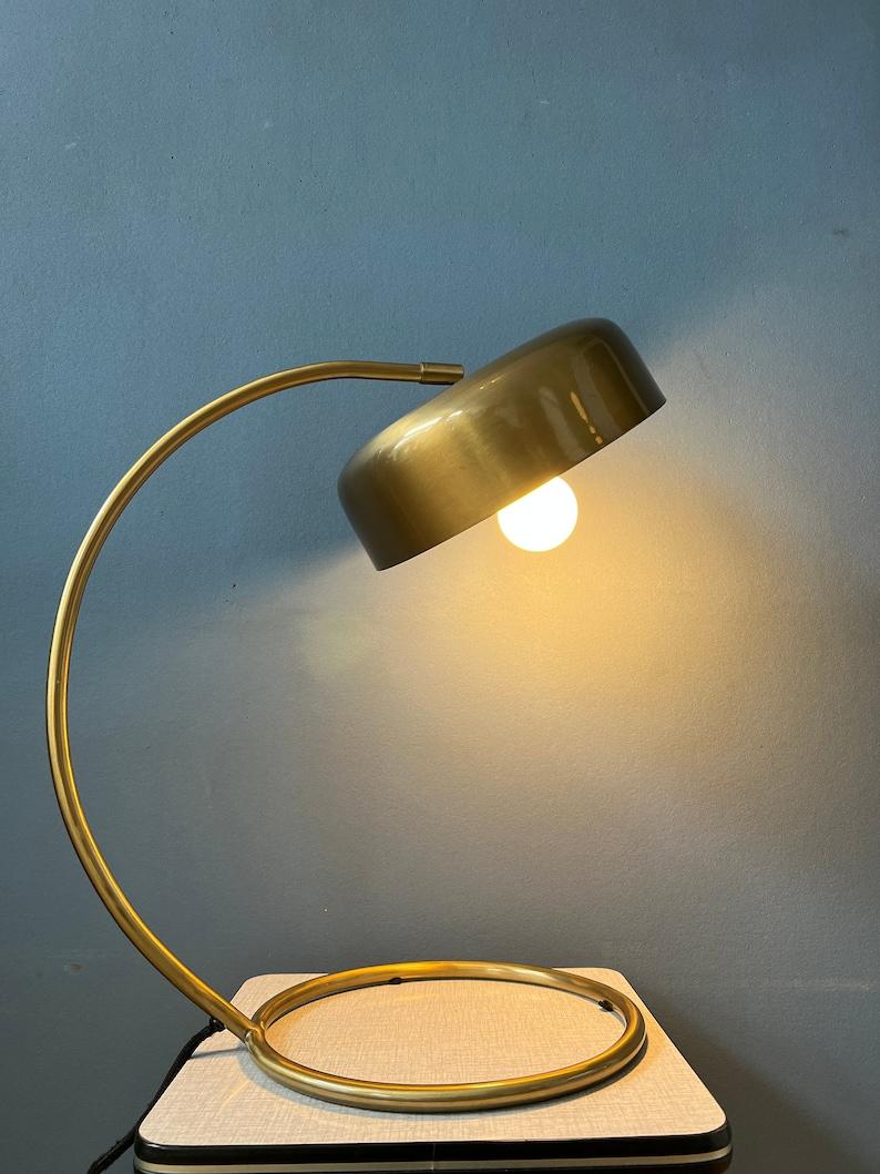 Mid century nicely shaped desk lamp in brass colour. The lamp has a thick lacquer and has a black colour underneath the shade. The shade can be easily turned in different directions. The lamp has a switch on the base. It requires a E27/26 bulb and