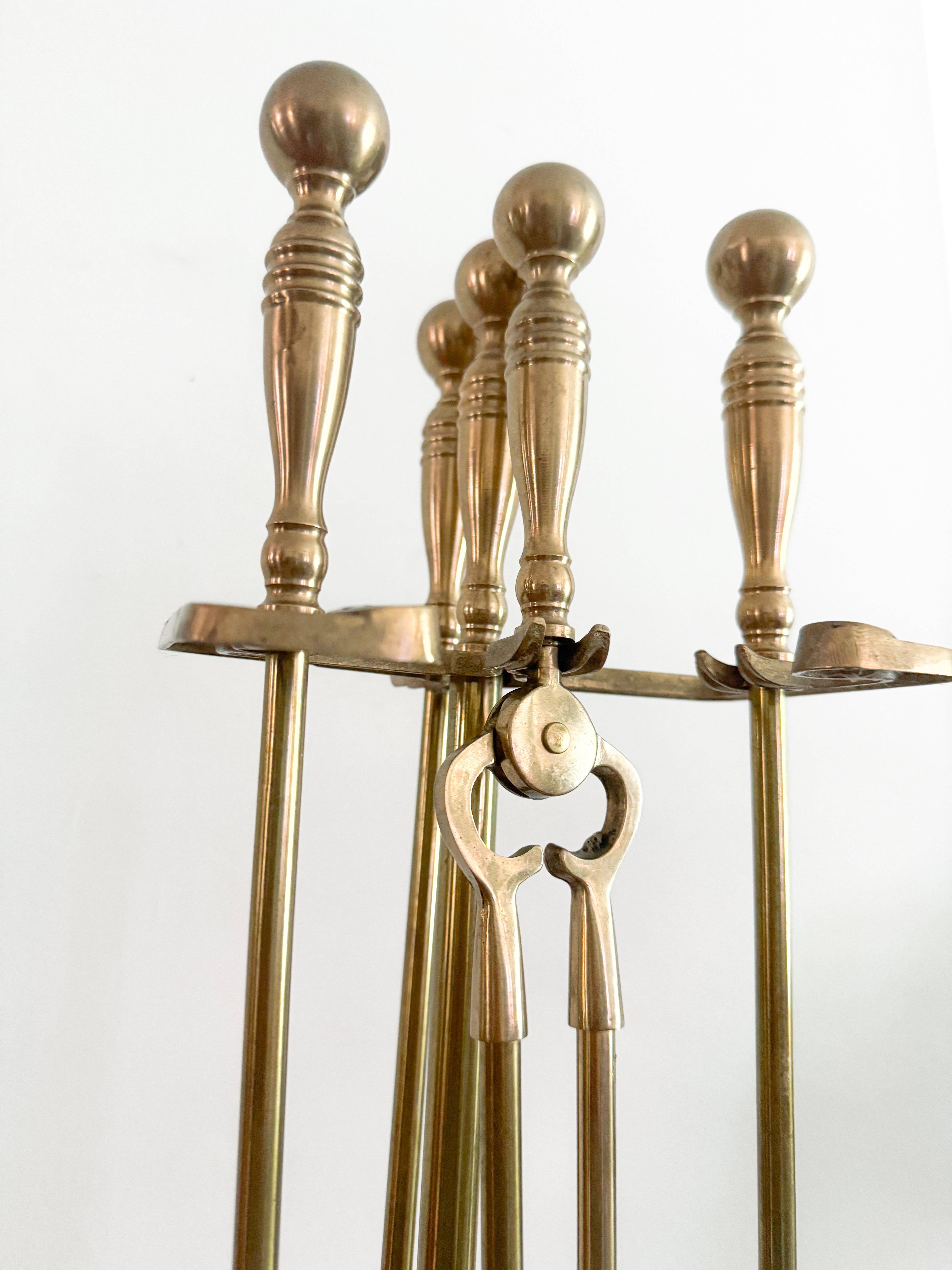 Un refinado juego de herramientas para chimenea de latón macizo de mediados de siglo, con las clásicas asas en forma de bola y elegantes detalles. Este diseño atemporal, de la década de 1950, incluye cuatro herramientas: pala, atizador, cepillo y