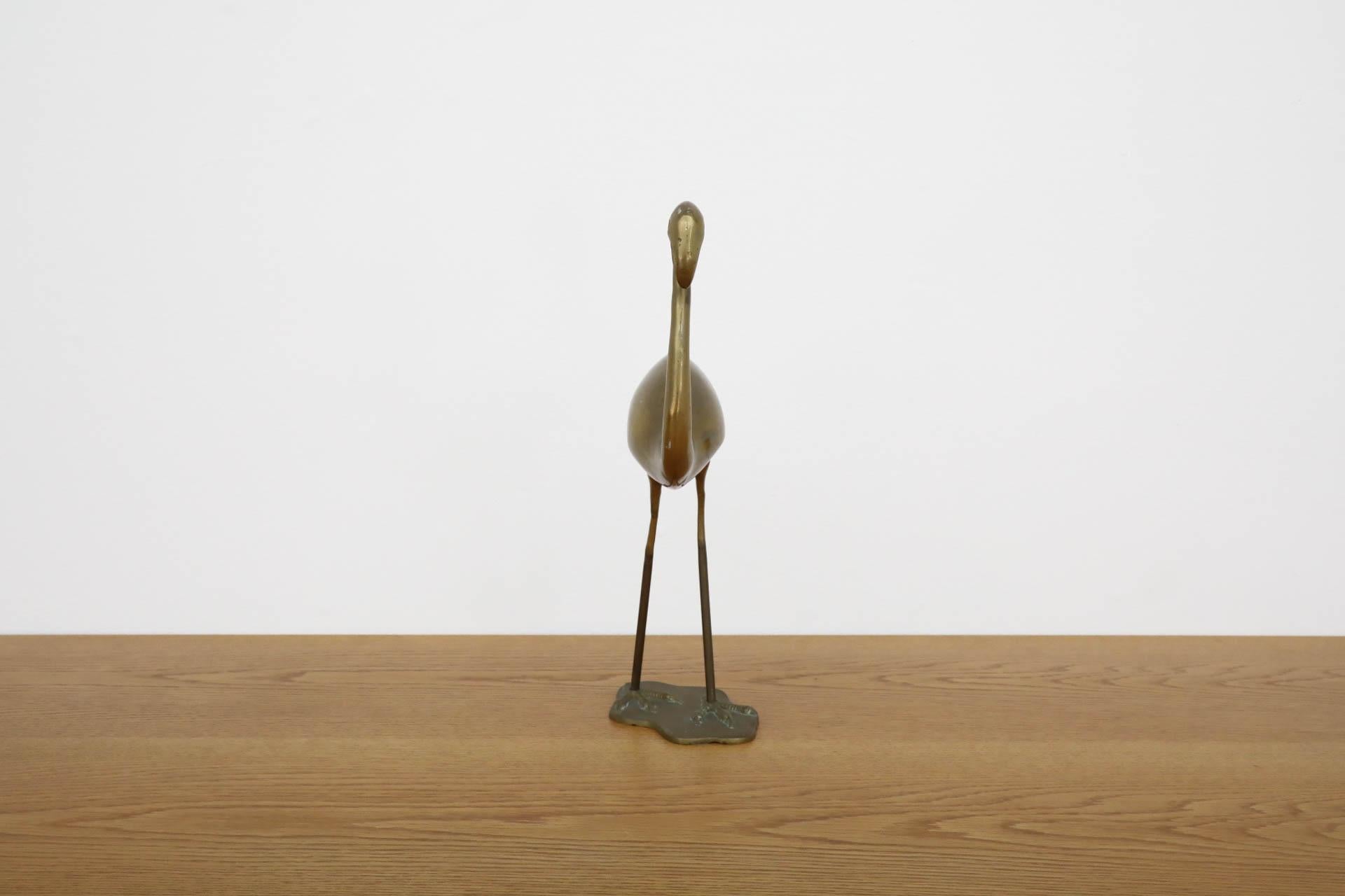 Mid-Century classically poised brass flamingo sculpture/statuette, unsigned. Hollow, as there is a faint rattling when shaken from loose pieces inside the sculpture. Base can be unscrewed. Has some visible patina and scratching that is consistent