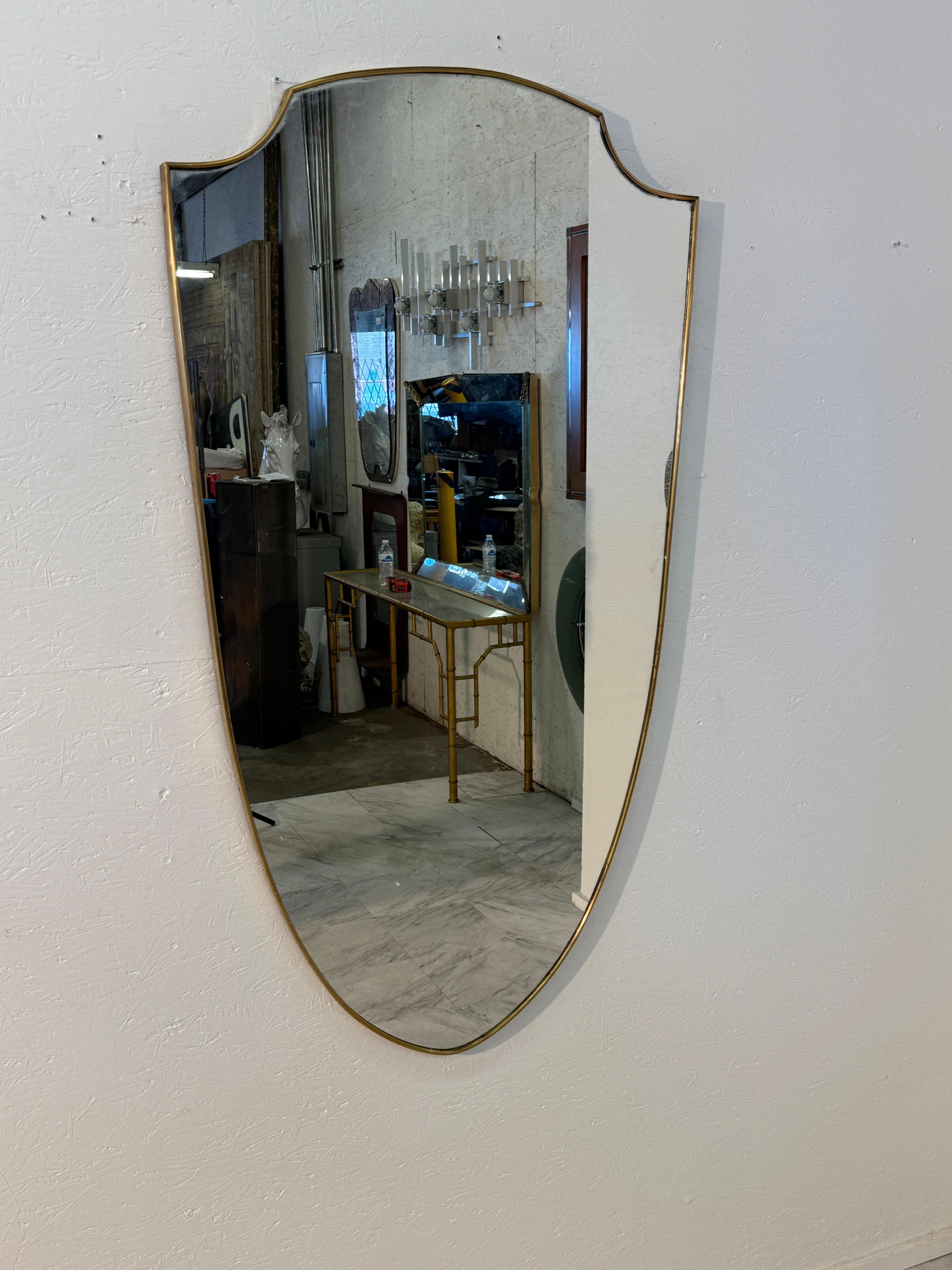Questo elegante specchio da parete presenta un'inconfondibile silhouette a forma di scudo, incorniciata da un sottile ottone che ha sviluppato una calda patina con l'età. Il piano curvo e la forma affusolata aggiungono un tocco aggraziato, quasi
