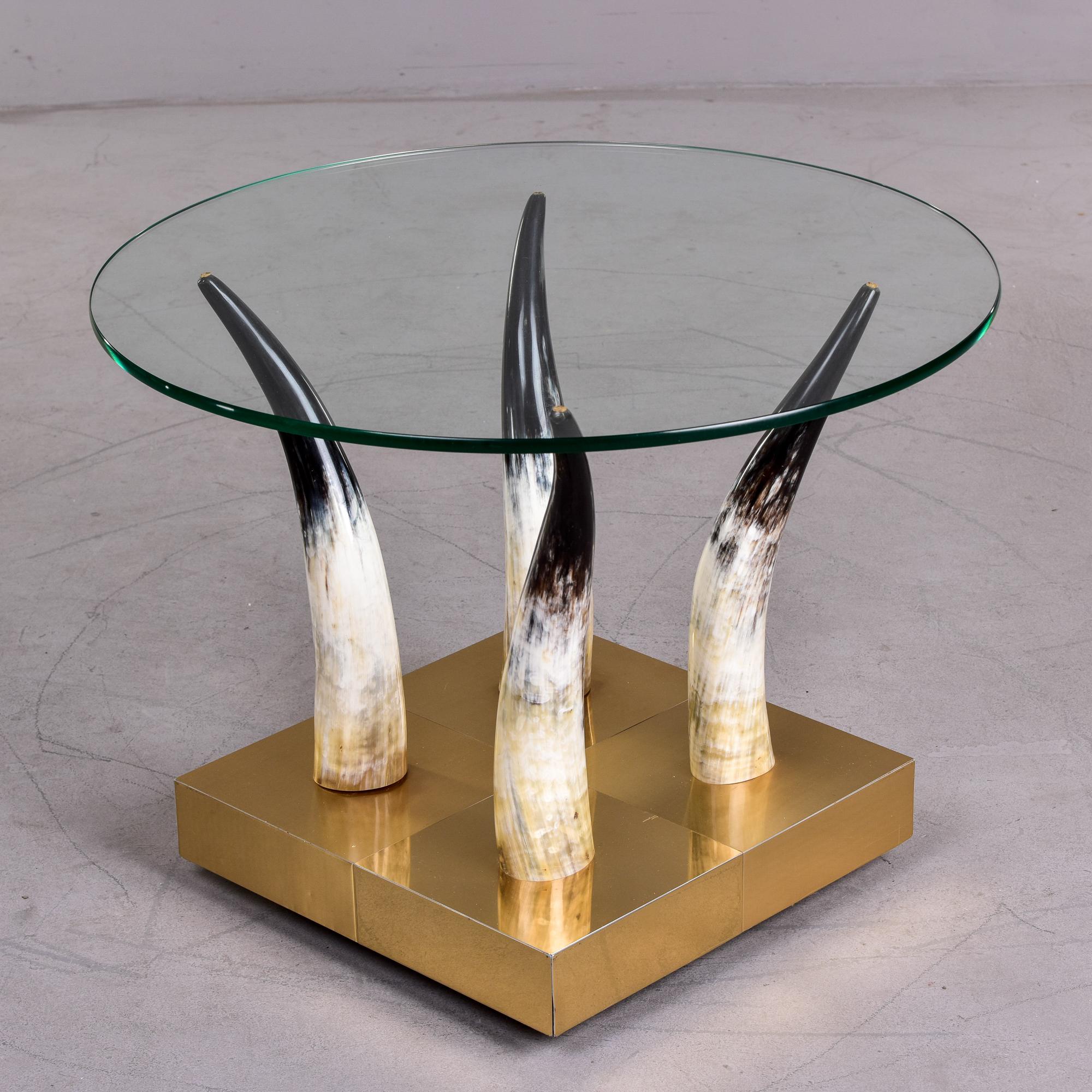 Circa 1970s side table has a brass covered base with casters and steer horns that support a clear glass table top. Unknown maker. Very good vintage condition with minor scattered surface wear.