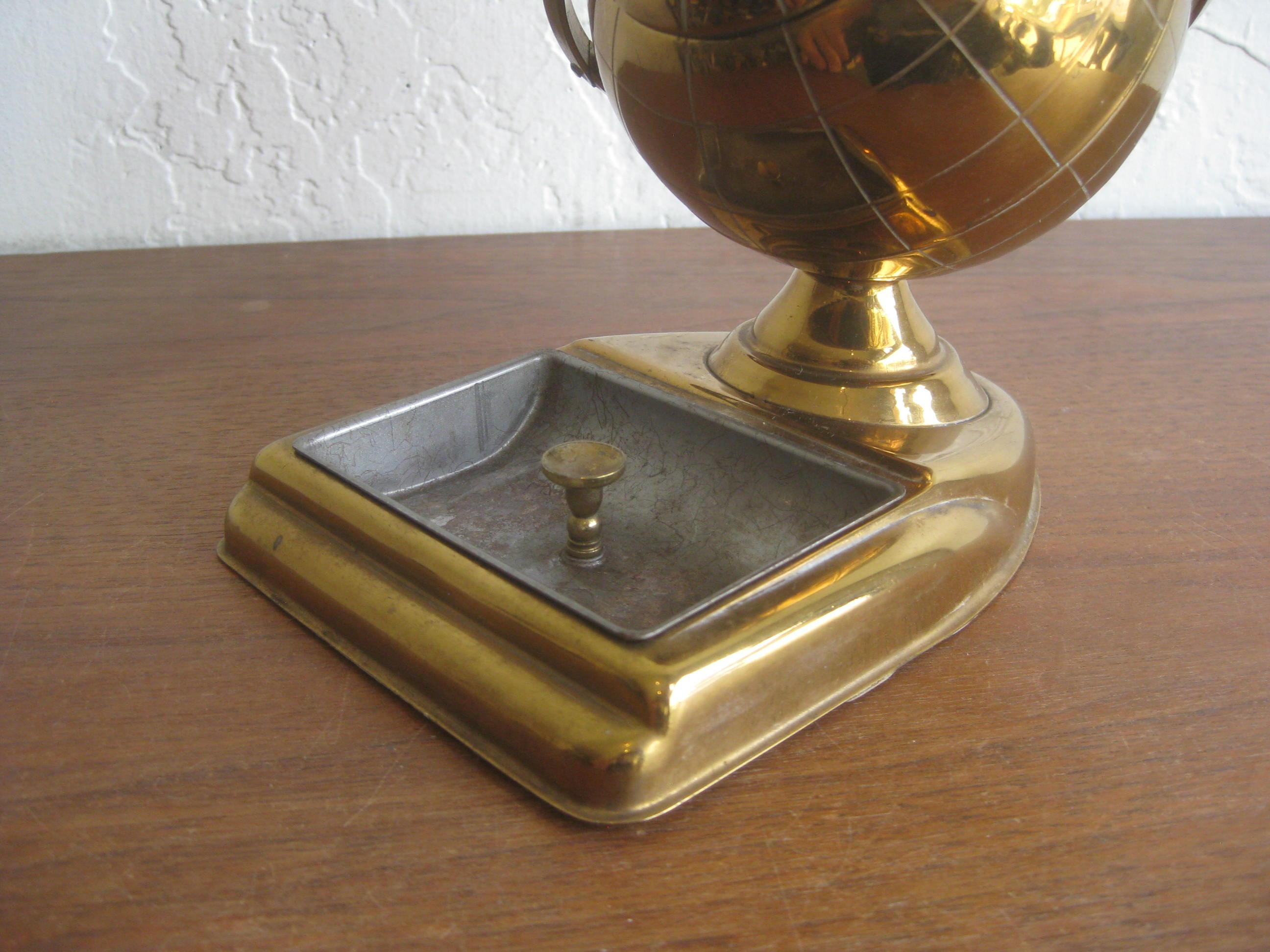 Brass figural globe cigarette holder and ashtray caddy, circa 1950s. Would make a great office desk accessory. Wonderful midcentury design. Nice patina and could polish up if desired. Opens as it should to store cigarettes inside the globe. In very