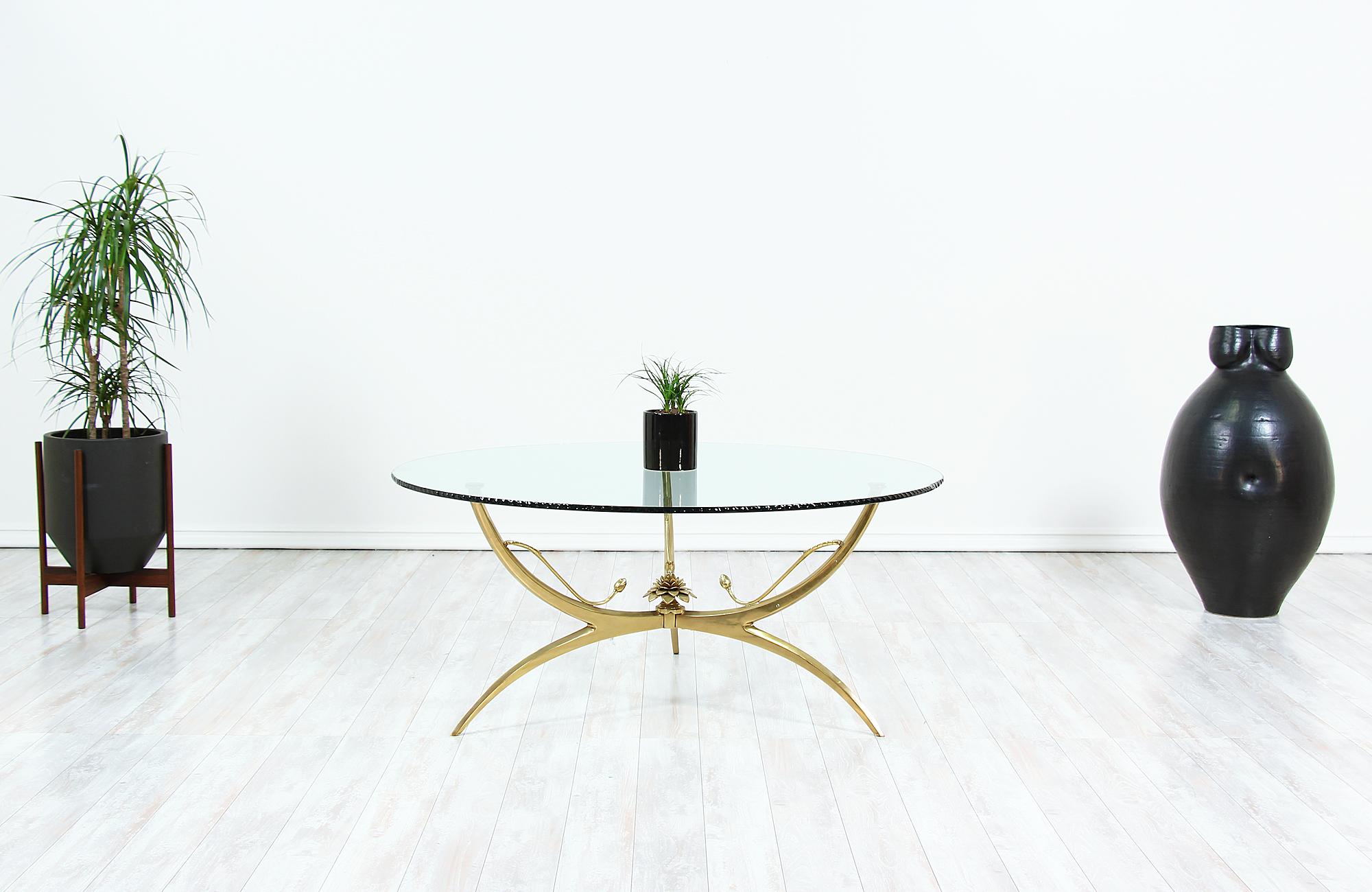 Elegant coffee table designed and manufactured in the United States, circa 1970s. This beautiful table features a lotus flower and bud motif in the center with three legs supporting the original glass top, which features an artistic wave-edge