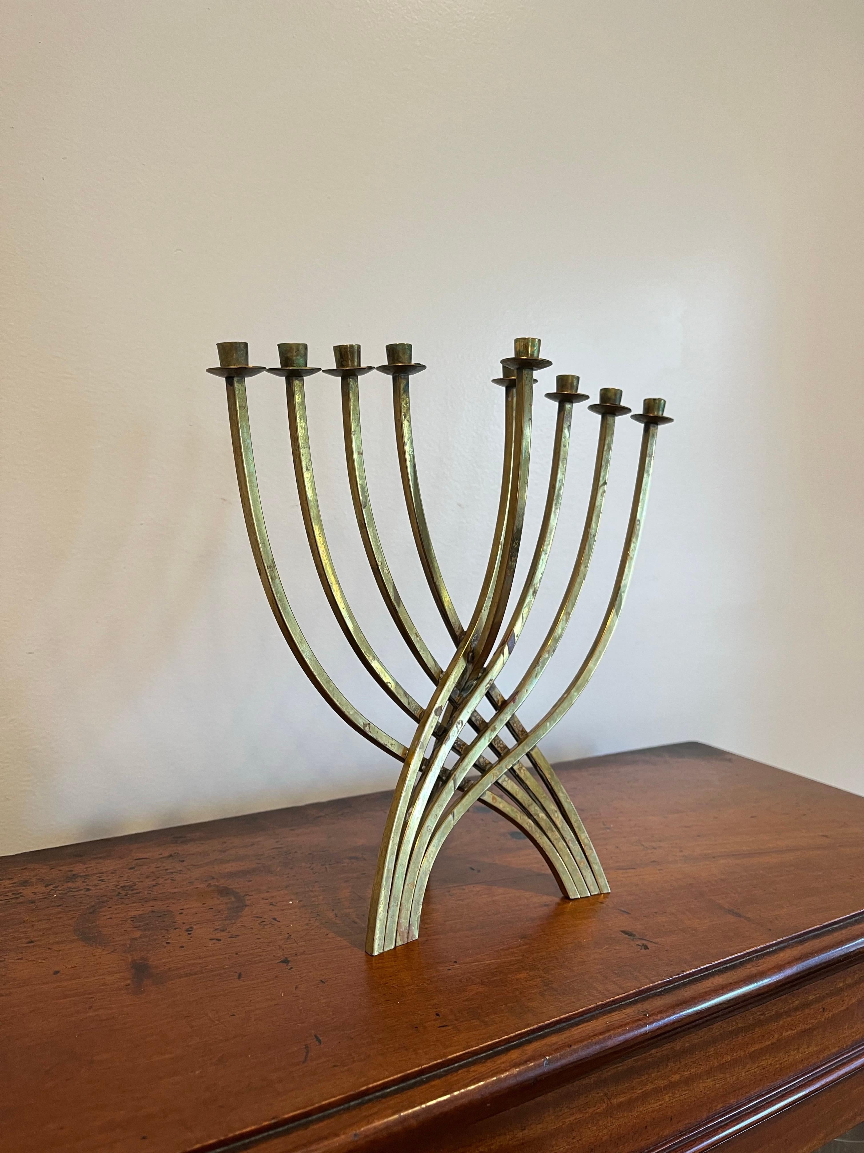 Menorah de latón de mediados de siglo a la manera de  Ludwig Wolpert. Libre de ornamentos innecesarios, esta lámpara moderna se reduce a lo esencial, con ramas curvas que se entrelazan y forman patas que, junto con el portavelas central, el shamash,