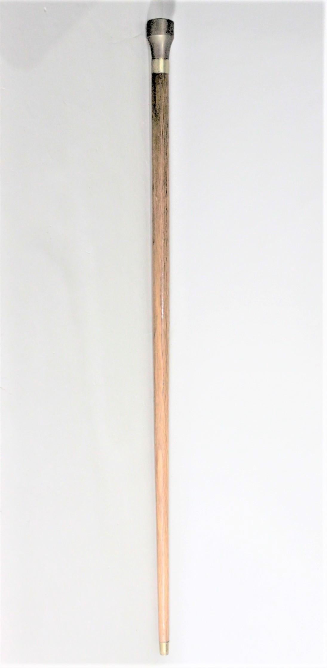 This vintage walking stick or cane is unsigned, but presumed to have been made in England in circa 1965 in the period style. The walking stick is made with a solid turned oak shaft with a brass top or pommel and brass end CAP. The brass handle of