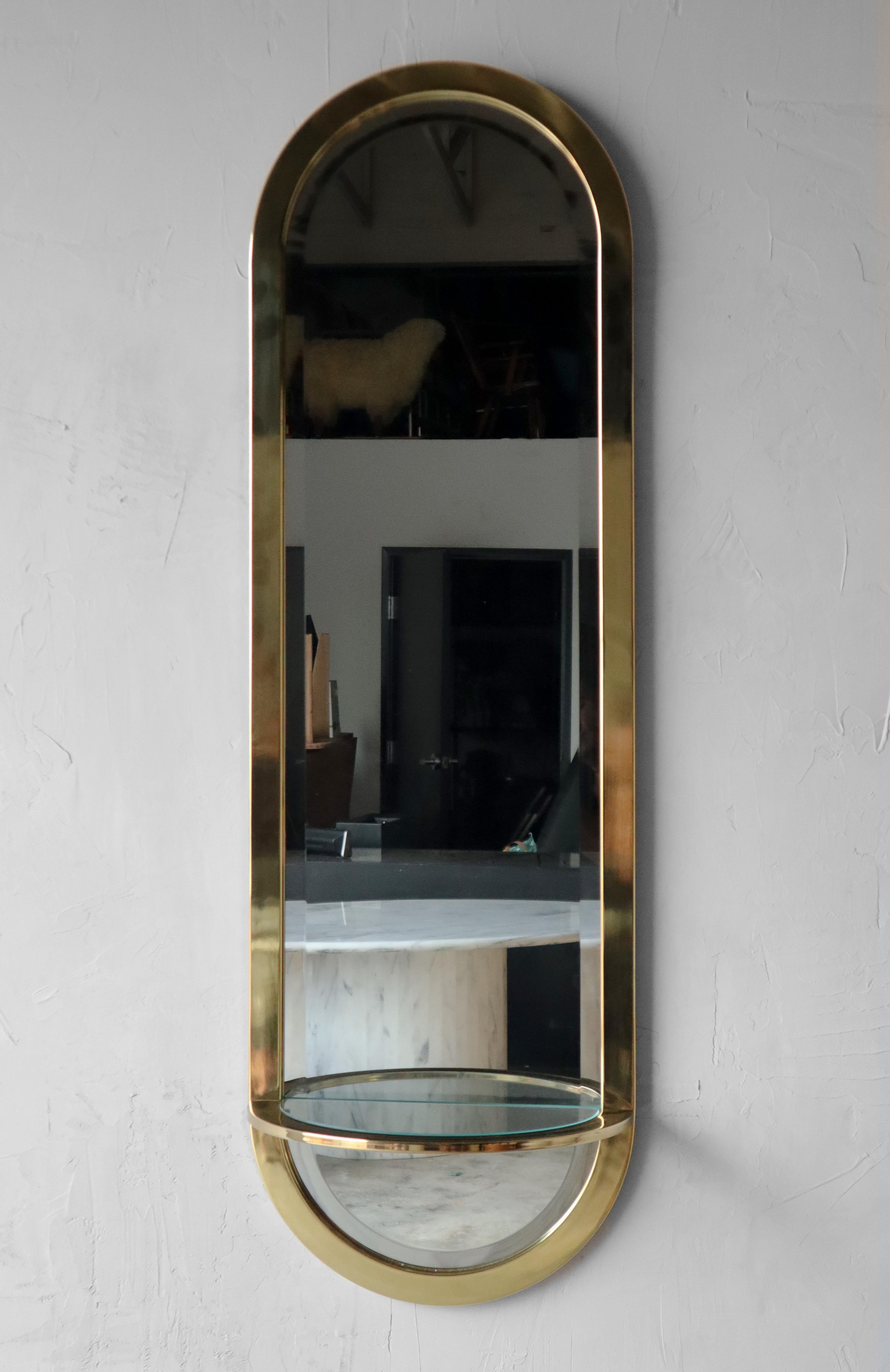 Beautiful Mid-Century Modern brass racetrack wall mirror with a demilune glass shelf, by Pace Collection.

Mirror is in excellent condition with no real damage to be noted.
