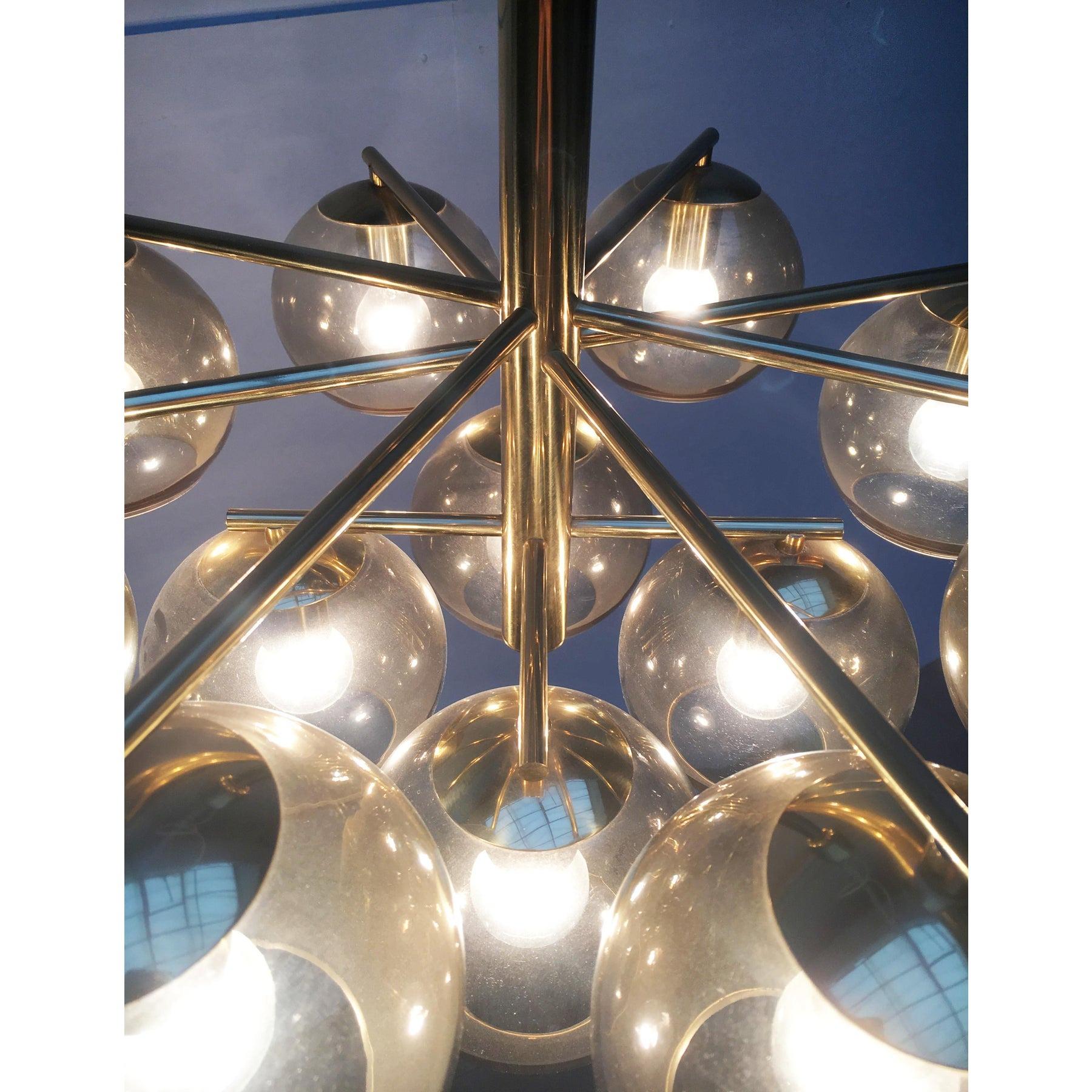Impressionante candeliere in ottone e vetro.

Questo lampadario combina un linguaggio di design minimalista e funzionale con l'aspetto imponente di un lampadario classico. Da un cilindro centrale nel nucleo partono radialmente sottili nastri