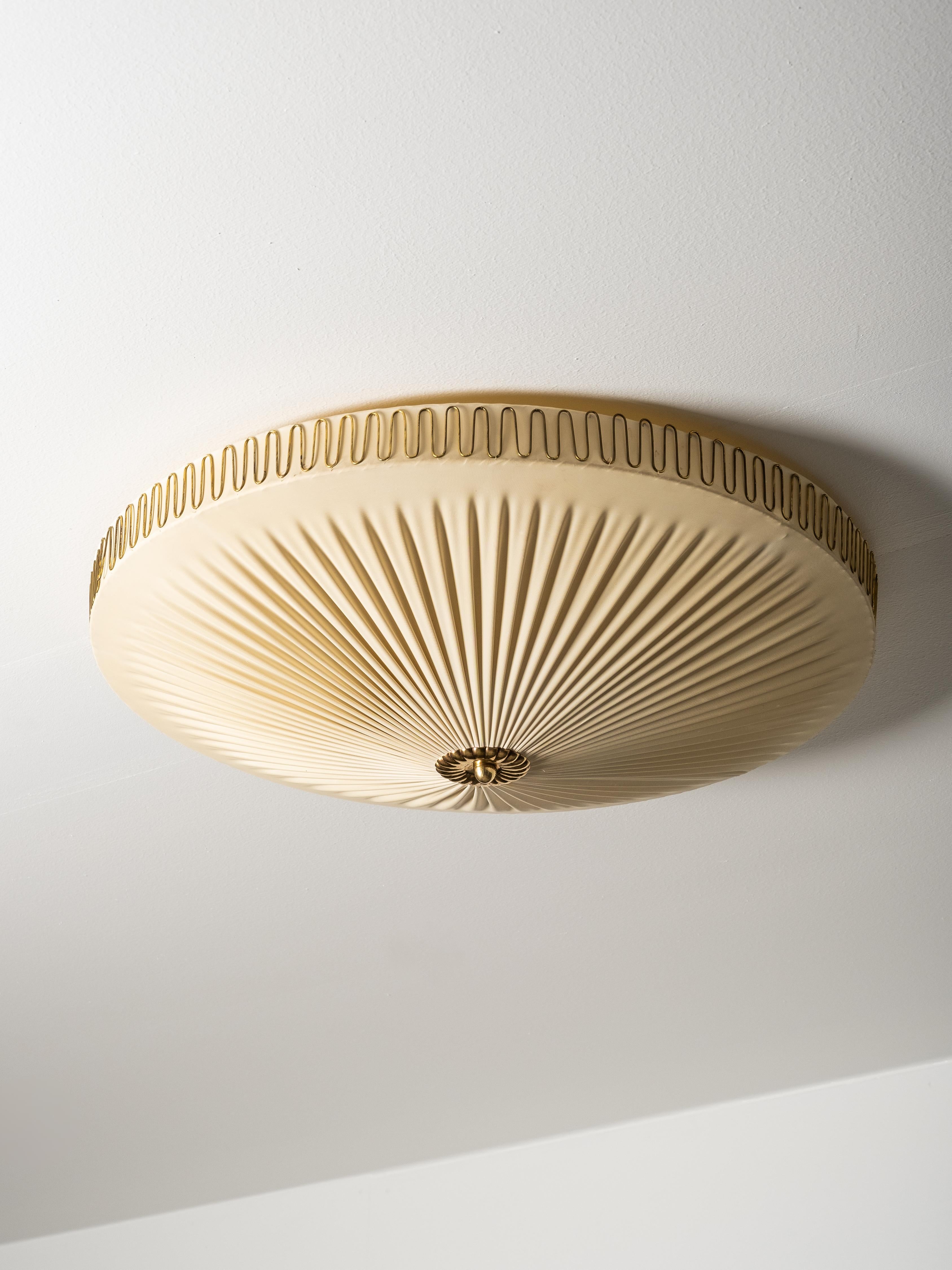 Elegant mid-century Model K5-40 ceiling light by Idman, Finland, 1950s. The design features a pleated synthetic textile diffuser stretched over a metal frame with decorative brass trim and finial, producing a soft, atmospheric glow.

While no