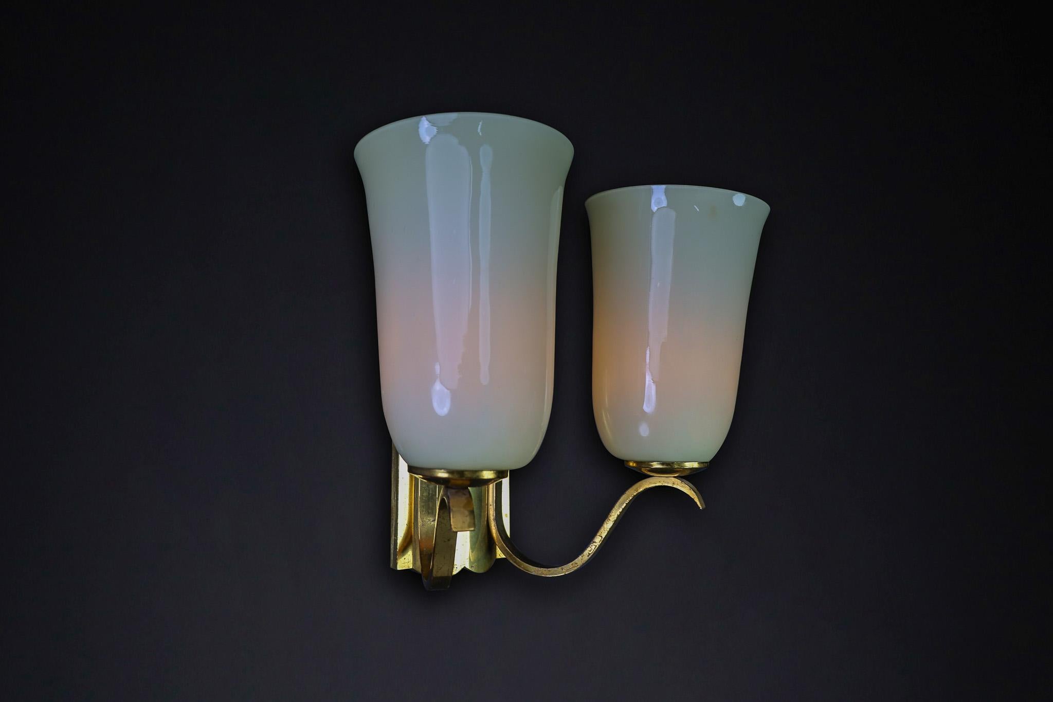 Mid-Century Brass Wall Light Sconce Opaline Glass Shades, Germany 1950s

This elegant mid-century wall sconce from the 1950s showcases exquisite German craftsmanship. It features gracefully curved brass arms and two tulip-shaped opaline glass