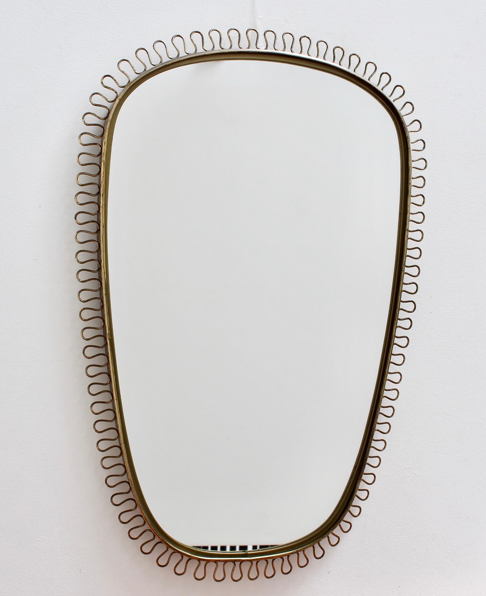 Brass wall mirror with decorative corona-effect surround by Josef Frank (circa 1950s). Original design, elegant presence and confident shape, this mirror is the centre of attention in any room. A characterful patina on the frame with dark patches
