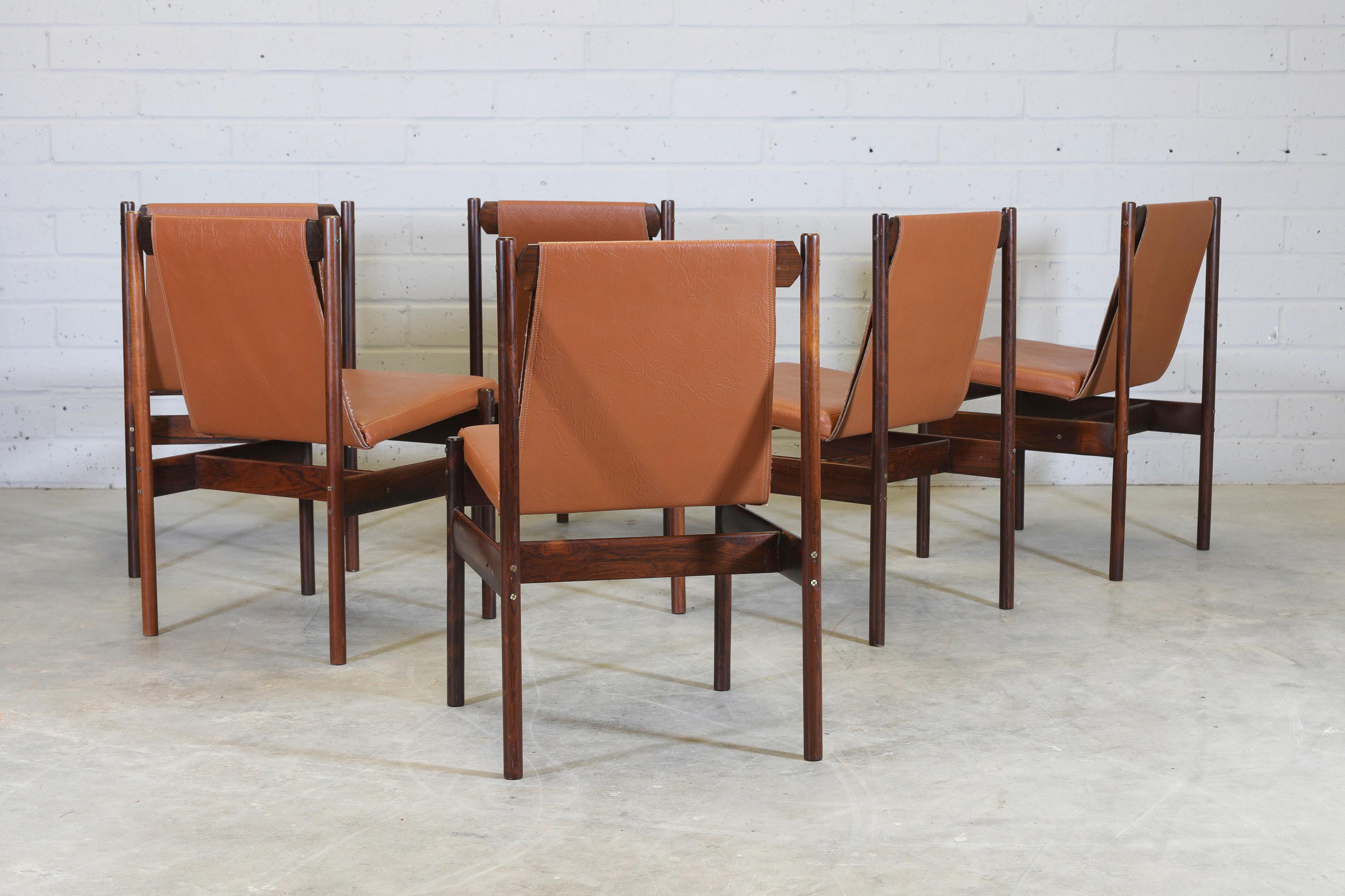 A set of six Brazilian hardwood dining chairs, designed by Novo Rumo, 1960s, each with a slung tan faux leather back, over a floating seat. Brazilian exotic hardwood frame with original brass screws and detailing.
The solid wood patterns and grain