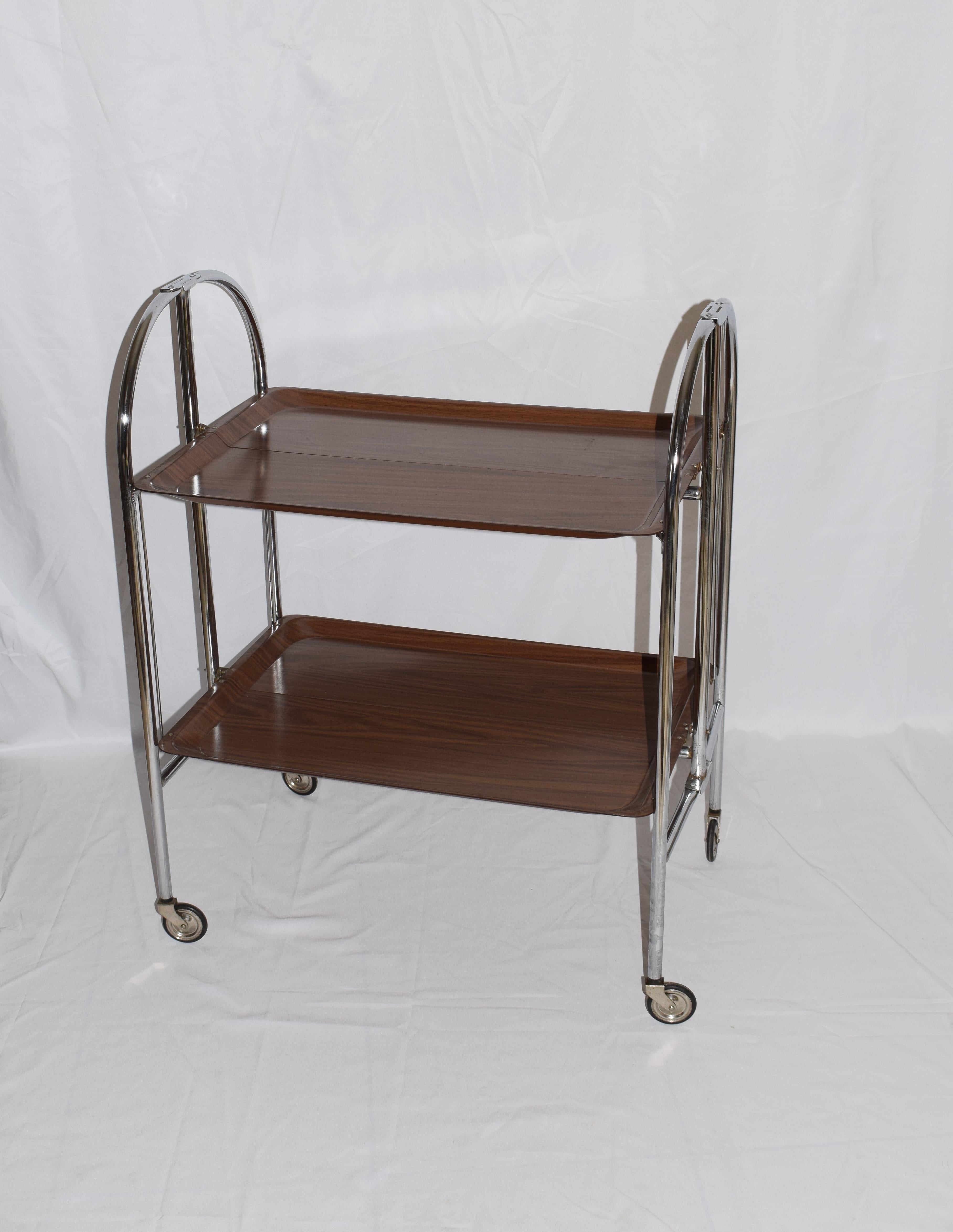 A mid-century Bremshey & Co German Dinette Trolley. Made of chrome & lamented wood. It folds into a smaller frame. Attribution mark on the wheels. Circa, 1950s

The trays are in a good condition. The chrome has a bit of rust on places but it has