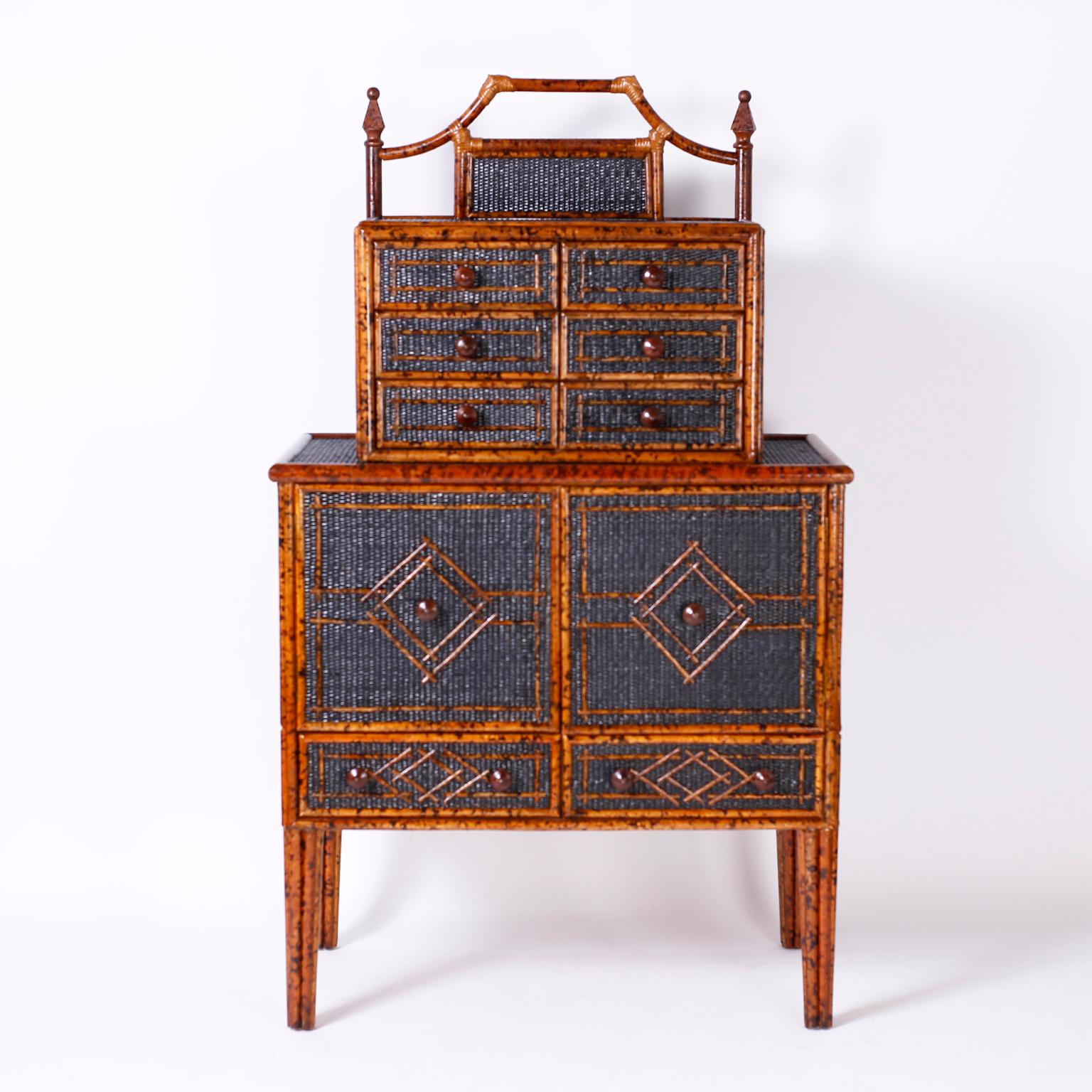 Handsome midcentury British Colonial chest on chest with six drawers above and a cabinet and two drawers below. Crafted with a faux bamboo frame having a faux tortoise finish, panels of black painted grasscloth under geometric designs and long