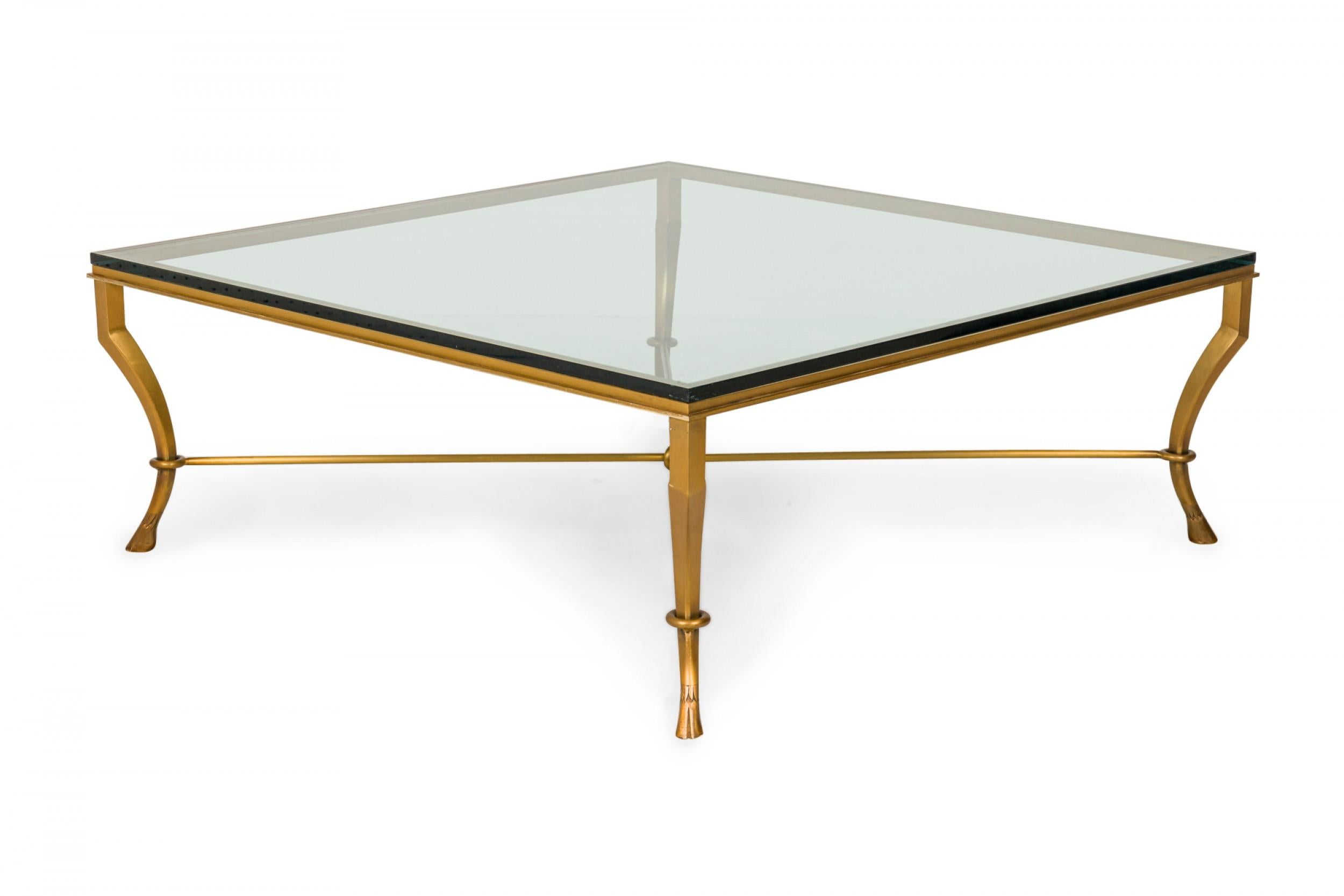 Mid-Century square coffee / cocktail table with a bronze frame with curved legs ending in hoof feet and an X-stretcher base, supporting a thick clear glass tabletop.
