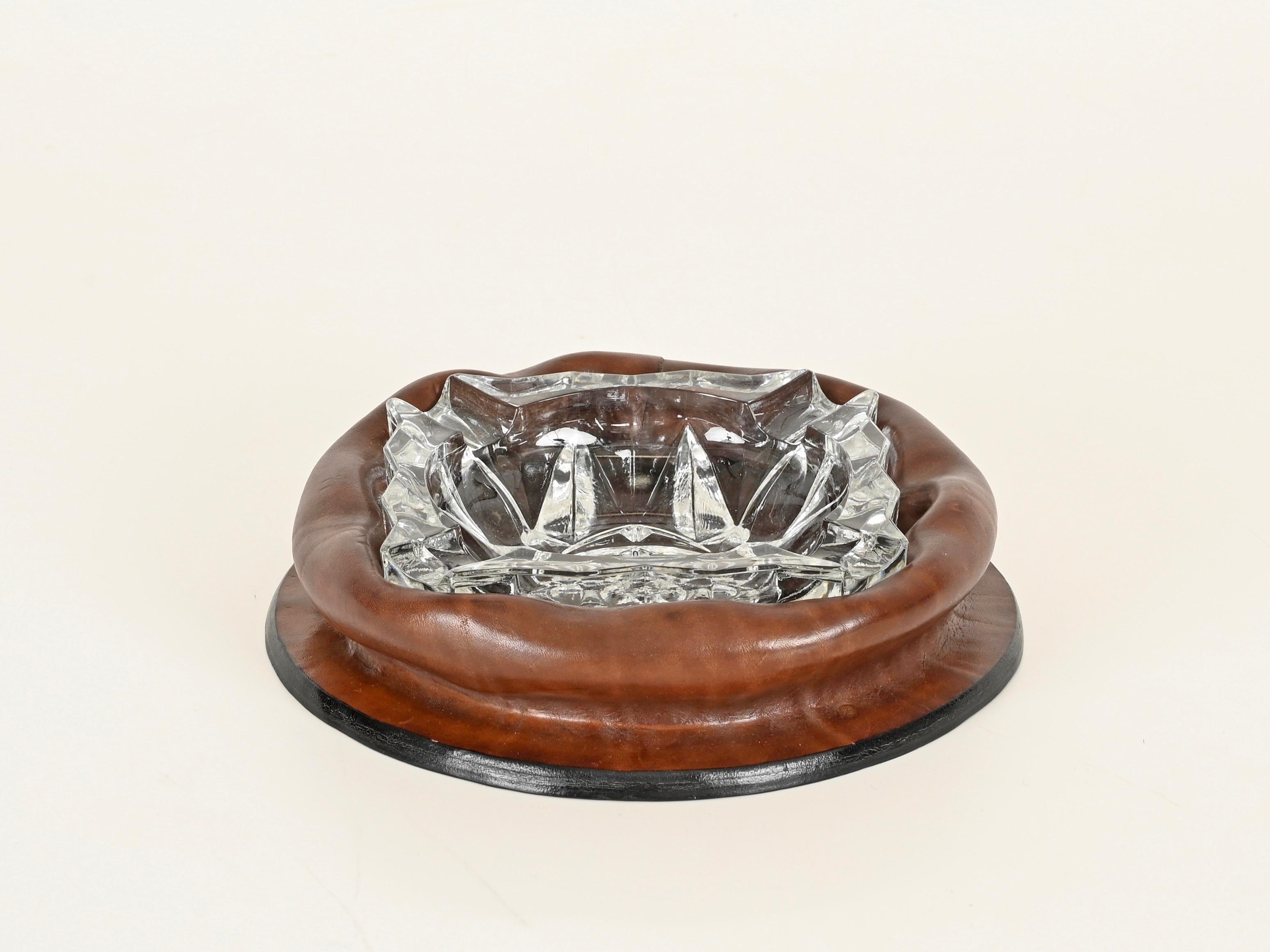 Spectaculaire cendrier du milieu du siècle, entièrement réalisé en cuir brun épais et incurvé et en verre de cristal taillé. Cette pièce élégante a été produite en Italie dans les années 1950 et est signée sur le fond.

En très bon état, sans