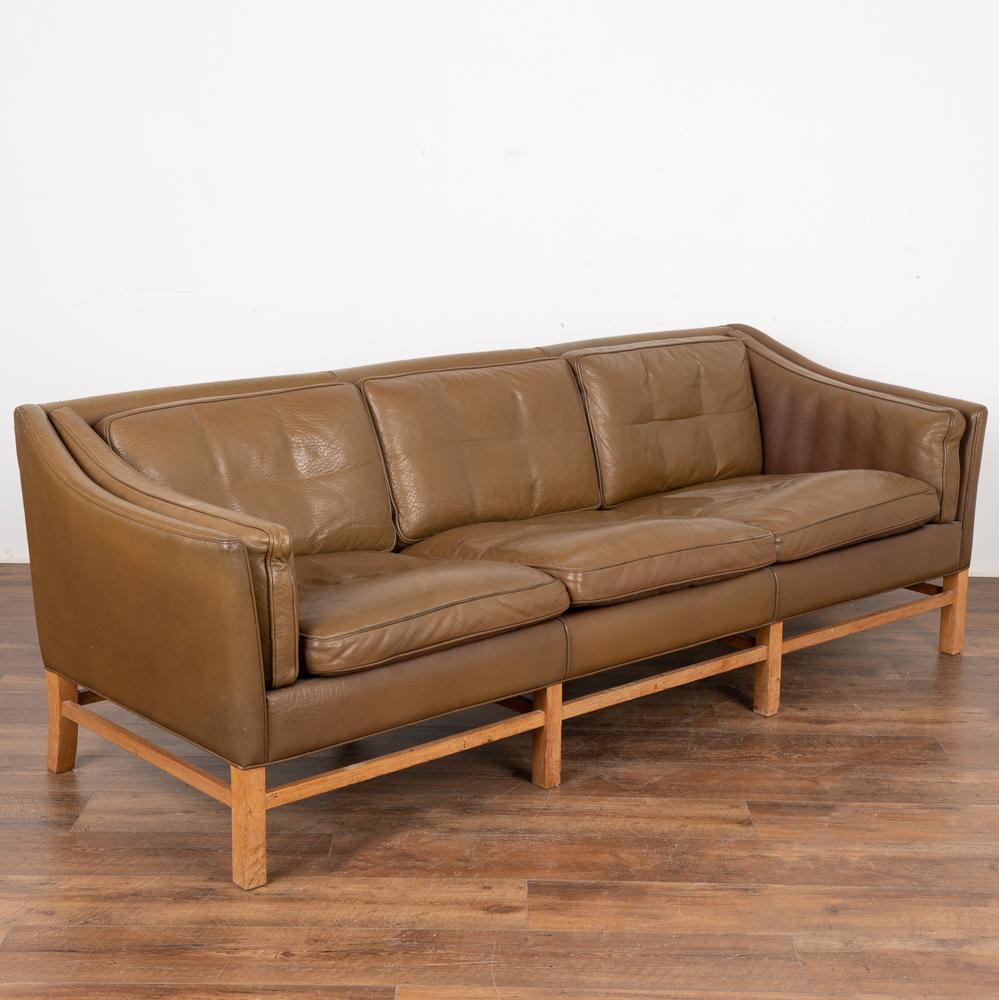 Mid-Century Modern brown leather three-seat sofa with removeable cushions and hard wood frame.
The years of use are revealed in the aged patina of the leather, including impressions, scuffs/scratches, some discoloration, stains on seat cusions,