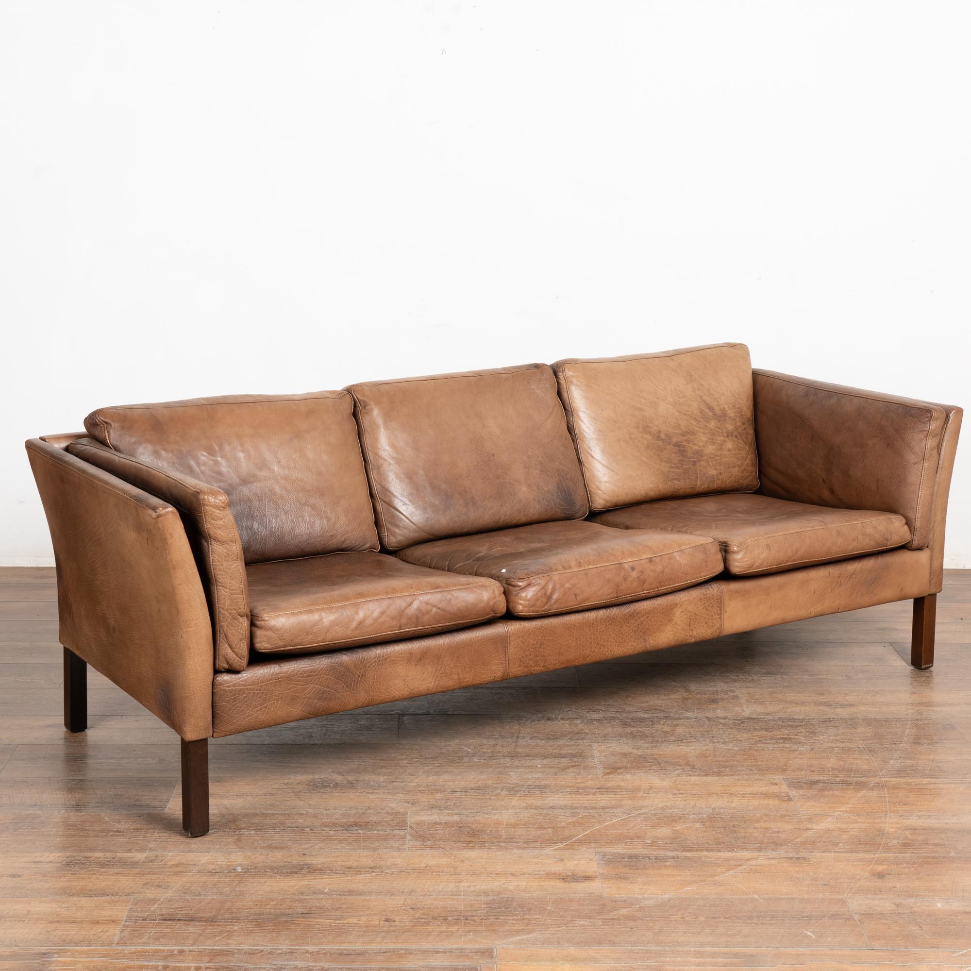 Modernes, braunes Ledersofa mit drei Sitzen, abnehmbaren Kissen und Hartholzrahmen.
Die Jahre des Gebrauchs zeigen sich in der gealterten Patina des Vintage-Leders, einschließlich Eindrücke, Schrammen/Kratzer, Verfärbungen, Flecken, mehrere