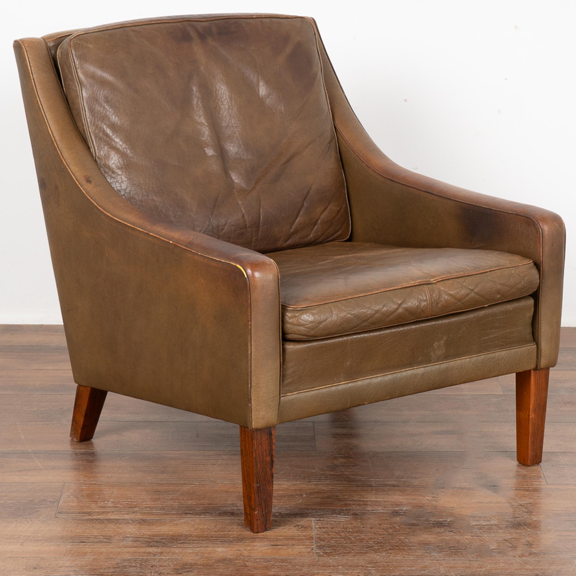 Mid-century modern brown leather arm chair resting on hard wood feet.
Clean modern design with sloping squared arms and removable cushions; these chairs sit comfortably .
Sold in vintage used condition. Leather shows typical signs of wear including