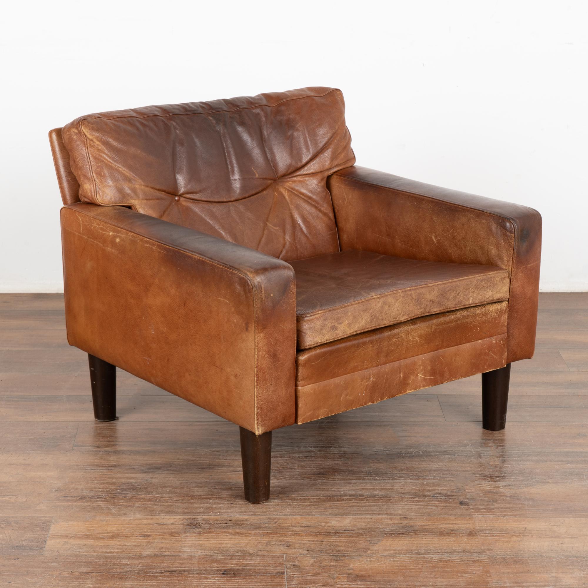 Mid-century modern brown leather arm chair resting on hard wood feet.
Cushions removeable with zipper closure.
Sold in vintage used condition; these chairs sit low. Leather shows typical age and use related signs of wear including multiple scuffs,