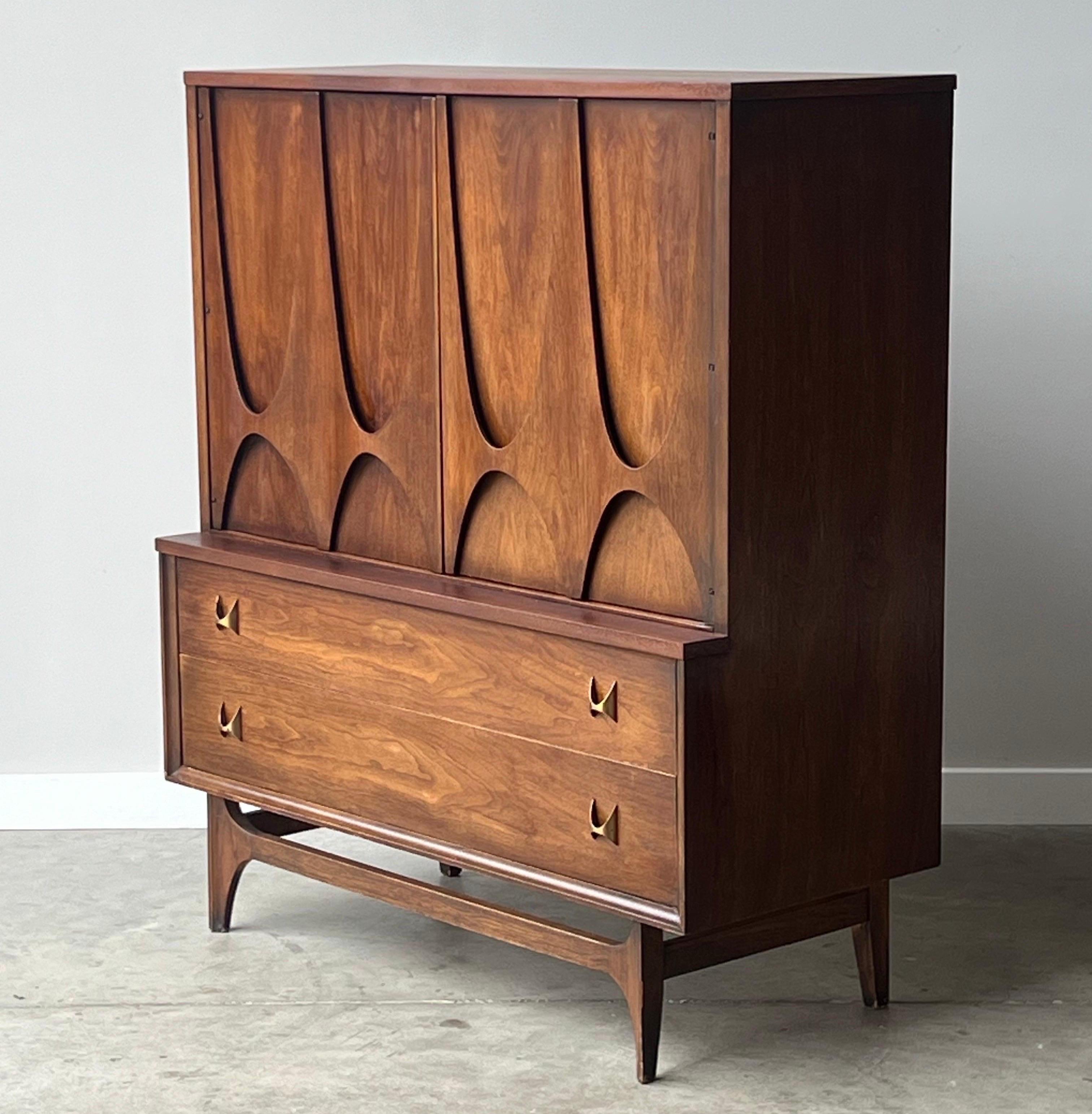 Mid-century gentleman’s chest or tall dresser manufactured by Broyhill and a part of the iconic Brasilia series. The entire Brasilia line share distinct sculpted arch details that mid-century enthusiasts love and often collect as a staple piece.